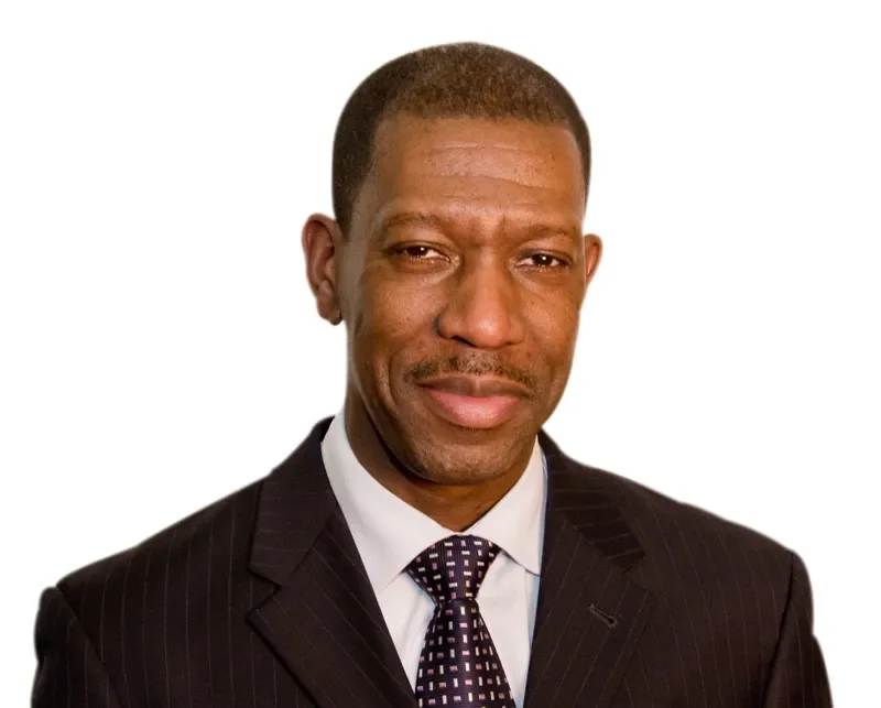 Un homme d'affaires africain en costume, souriant légèrement, fond blanc.