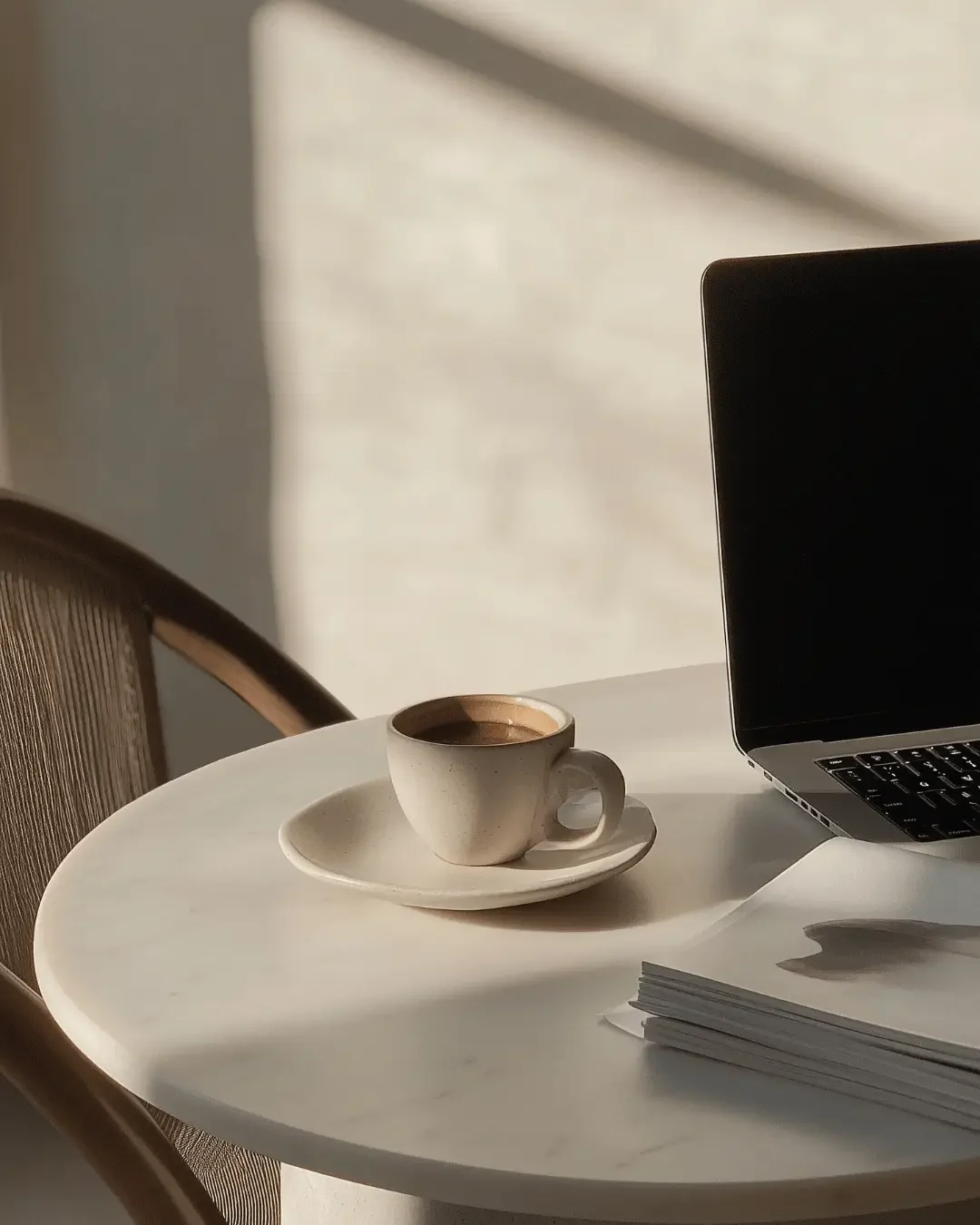 Coffee cup on a round table next to a laptop and stack of papers, representing bookkeeping focus and organized business workspace