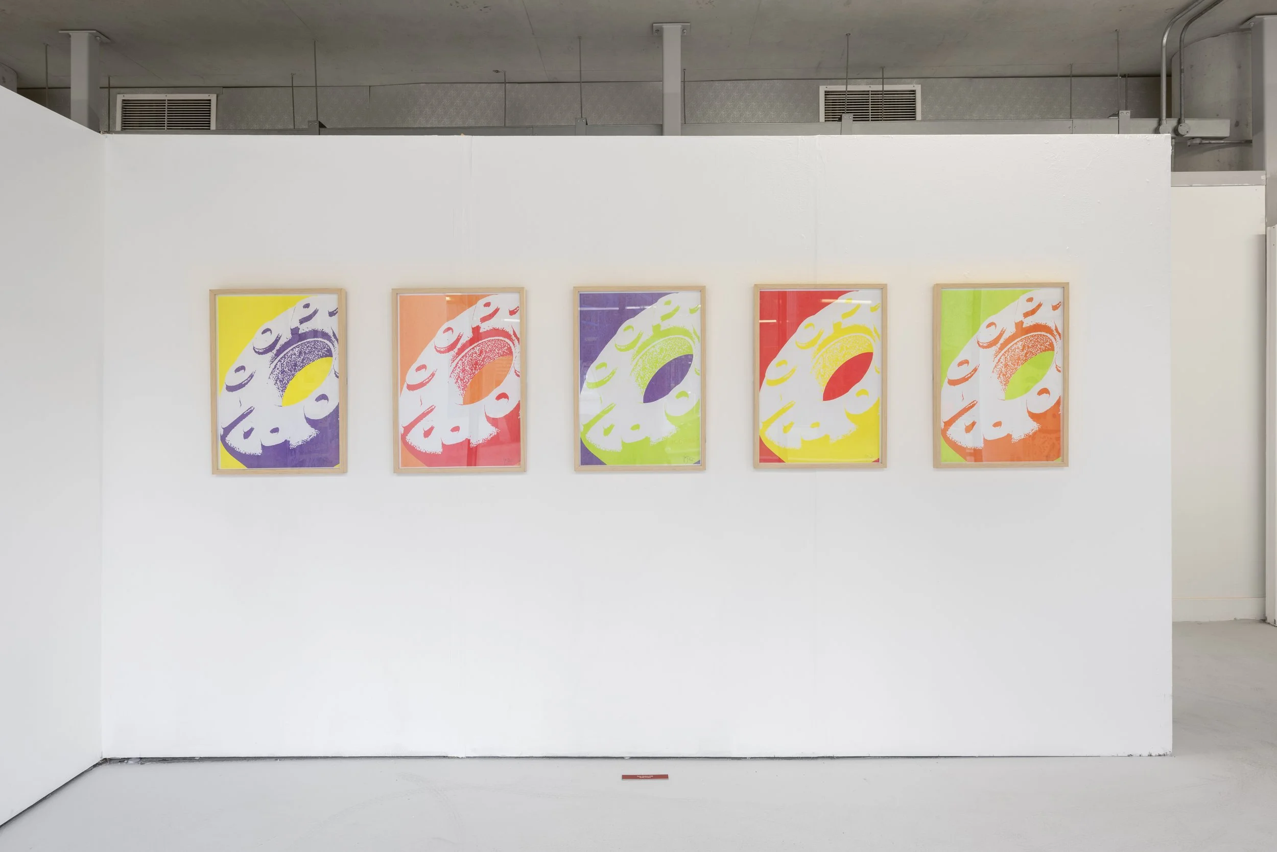 Exhibition photograph of a series of five multi-coloured prints in different bold colours, each depicting the same image of an enlarged ‘Fruit Loop’ sweet (a variant of a mint POLO). The fruit loop is inscribed with ‘Loop’ filling majority of the fra