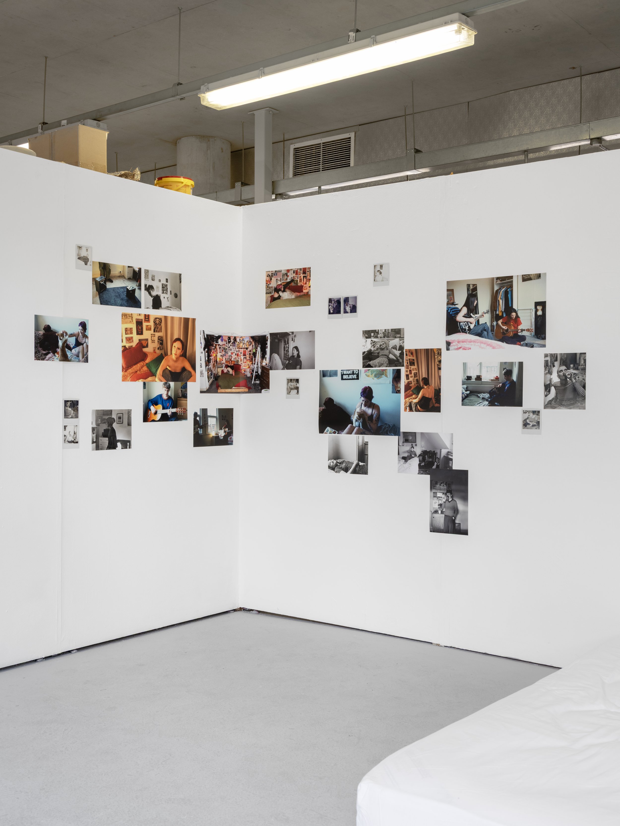 Image of Abbie Bruff's ‘Between Panic and Pleasure’ installed in ‘From my Bed’ exhibited in the corner of the white walled gallery. A photographic installation incorporating an array of images in both black and white and colour. Installed in a scatte