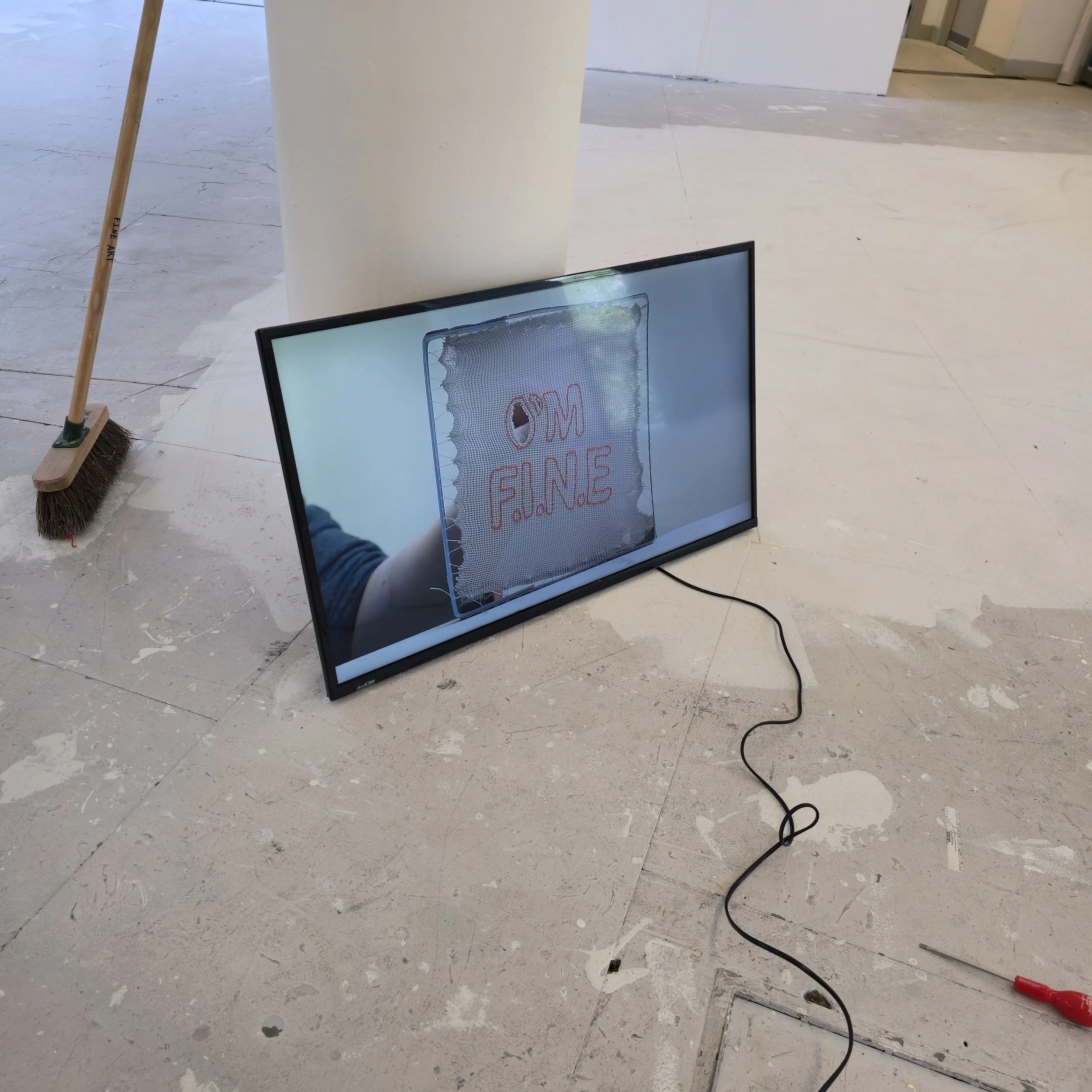 Installation of Stretched To Breaking Point 2026, 60 second film by Joanne Tiffany. A flat screen monitor lent against a pillar on the floor