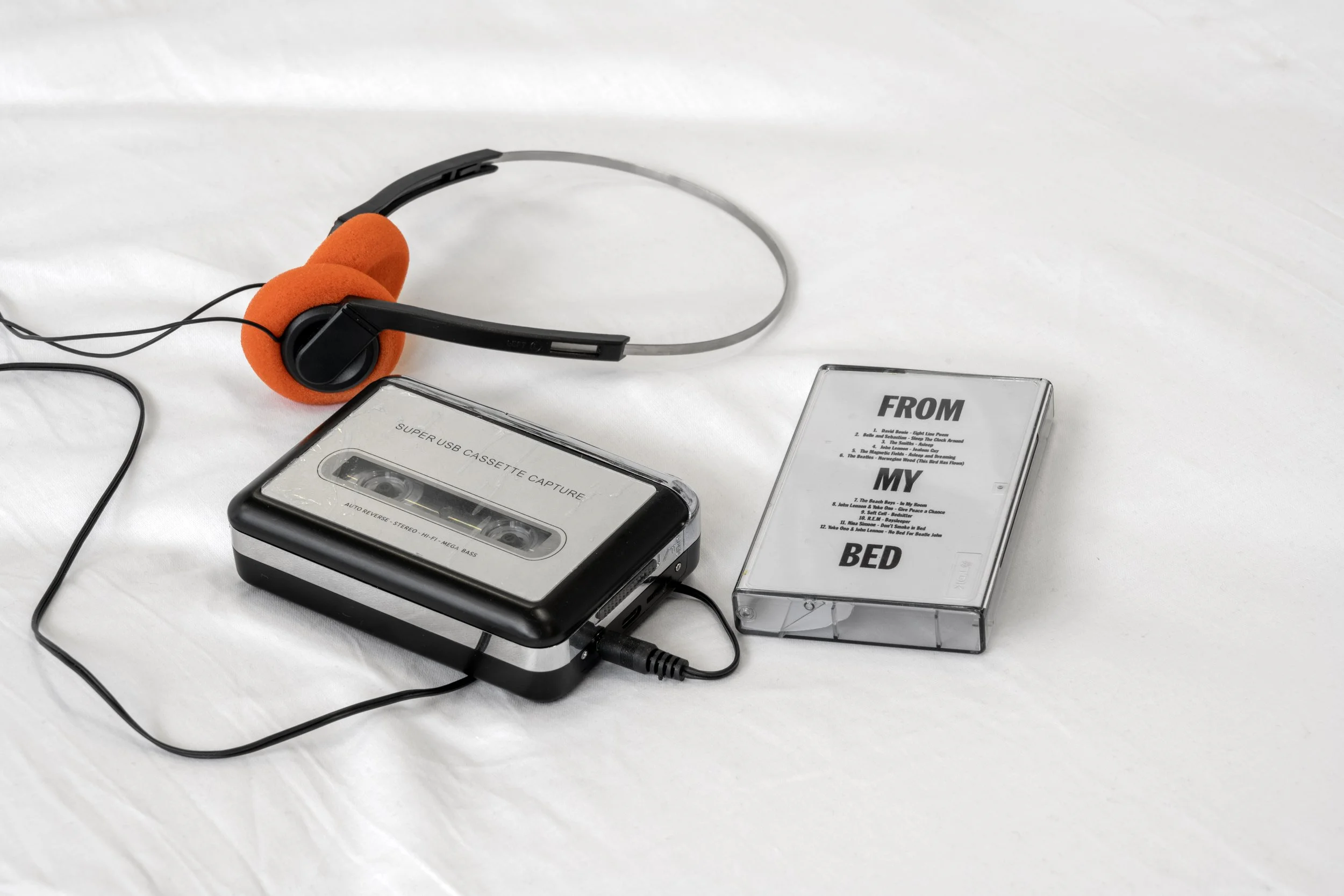 Close-up of Abbie Bruff and Alan Dunn's mix tape and cassette player with headset placed on the white sheet covered mattress.