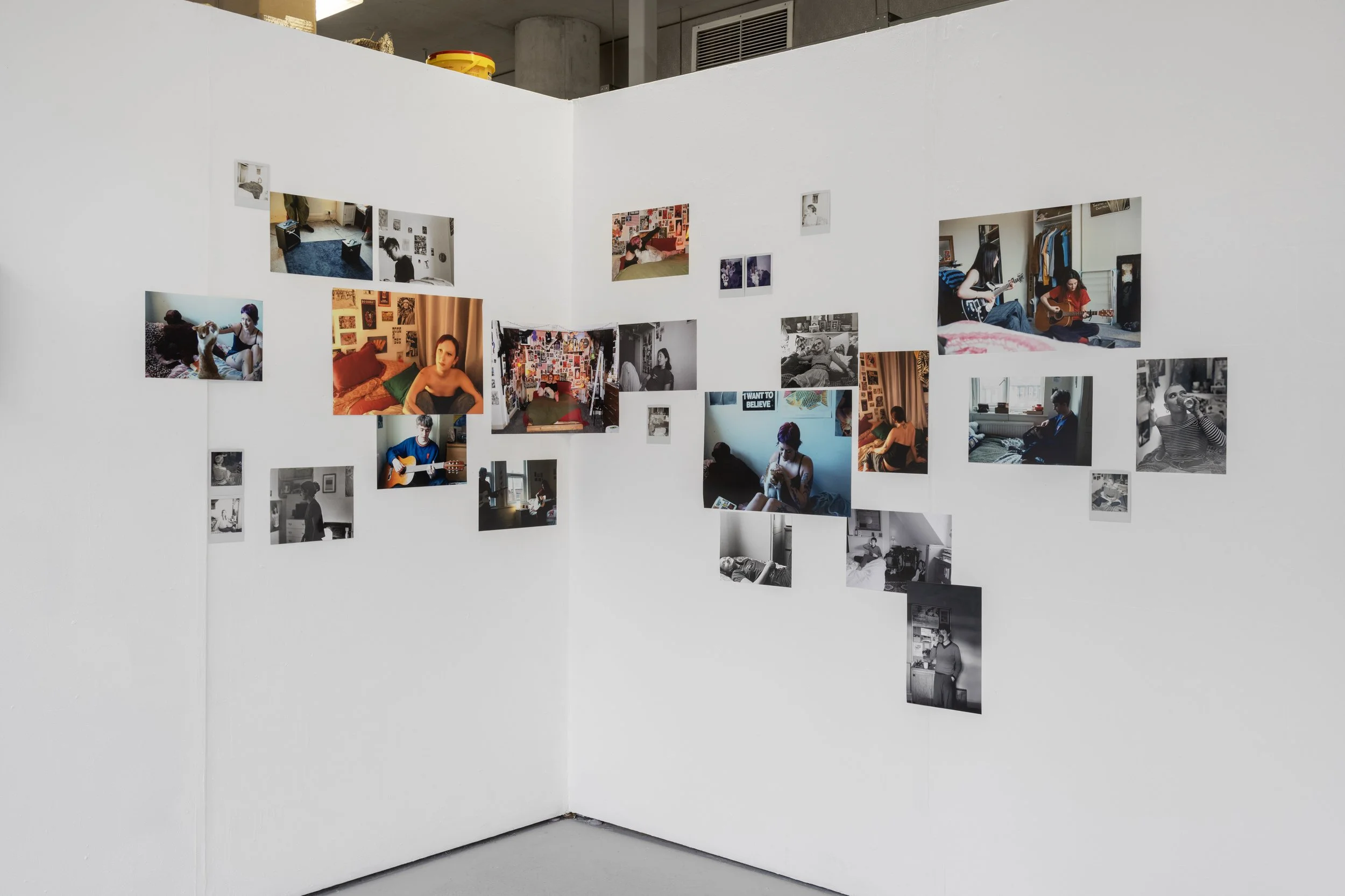 Image of Abbie Bruff's ‘Between Panic and Pleasure’ installed in ‘From my Bed’ exhibited in the corner of the white walled gallery. A photographic installation incorporating an array of images in both black and white and colour. Installed in a scatte