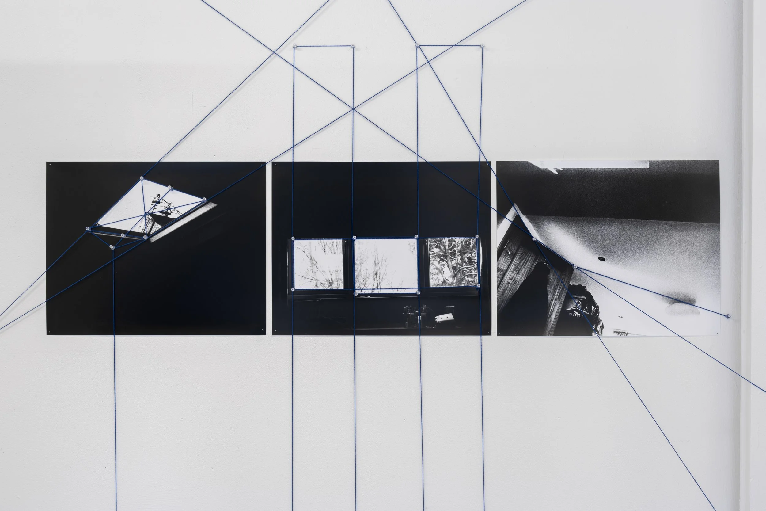 From My Bed Exhibition photograph of Liz Sayway's artwork against a white wall in the White Column gallery. The artwork comprises three separate black & white photographs, linked and covered with an overlaying network of webbed blue thread that conti