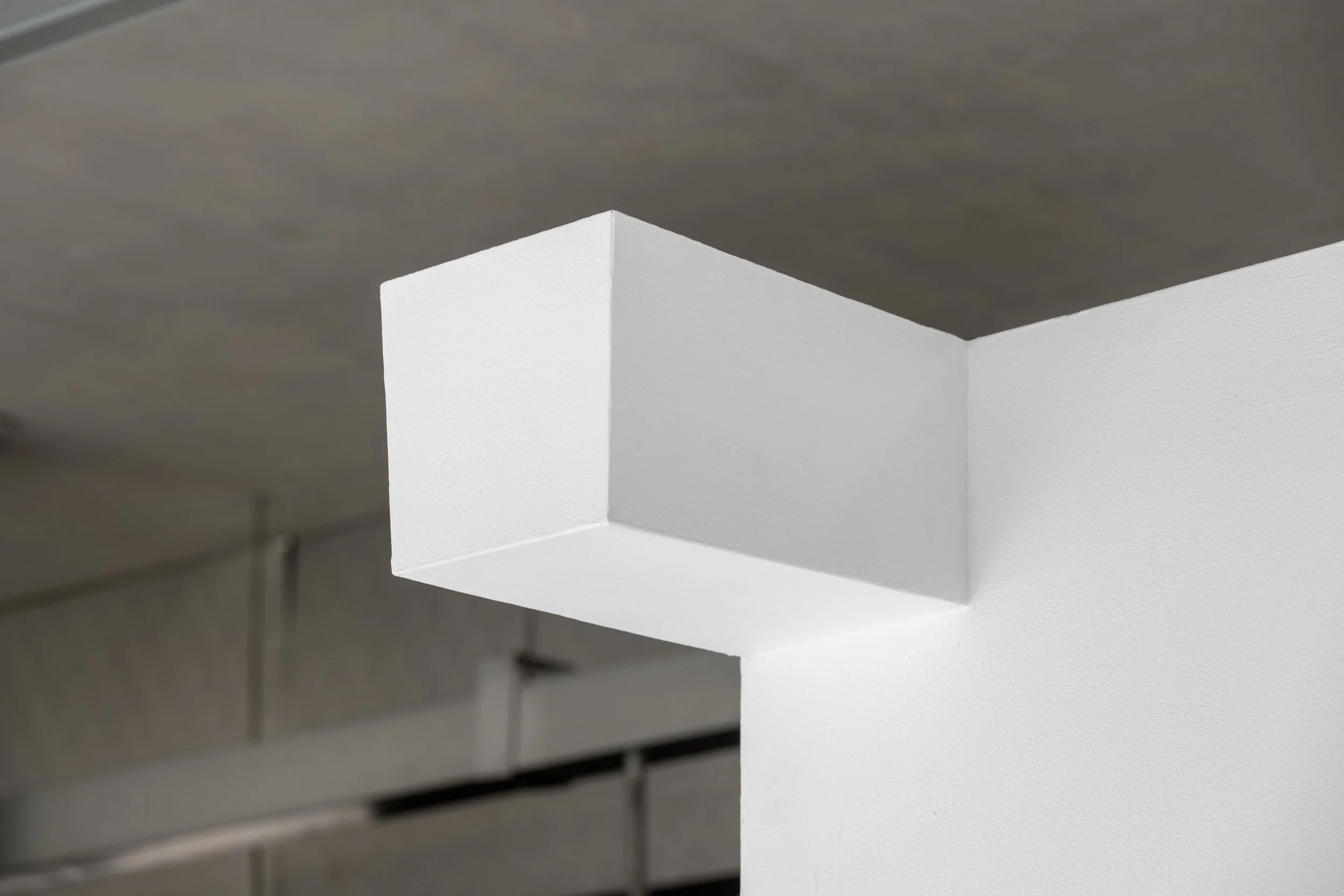Harry Meadley's artwork photographed high up on a white wall in the White Column space. A white shoe box sized form protrudes from the upper part of a white gallery wall. It is positioned so even a tall person would look up at it. The box’s surface i
