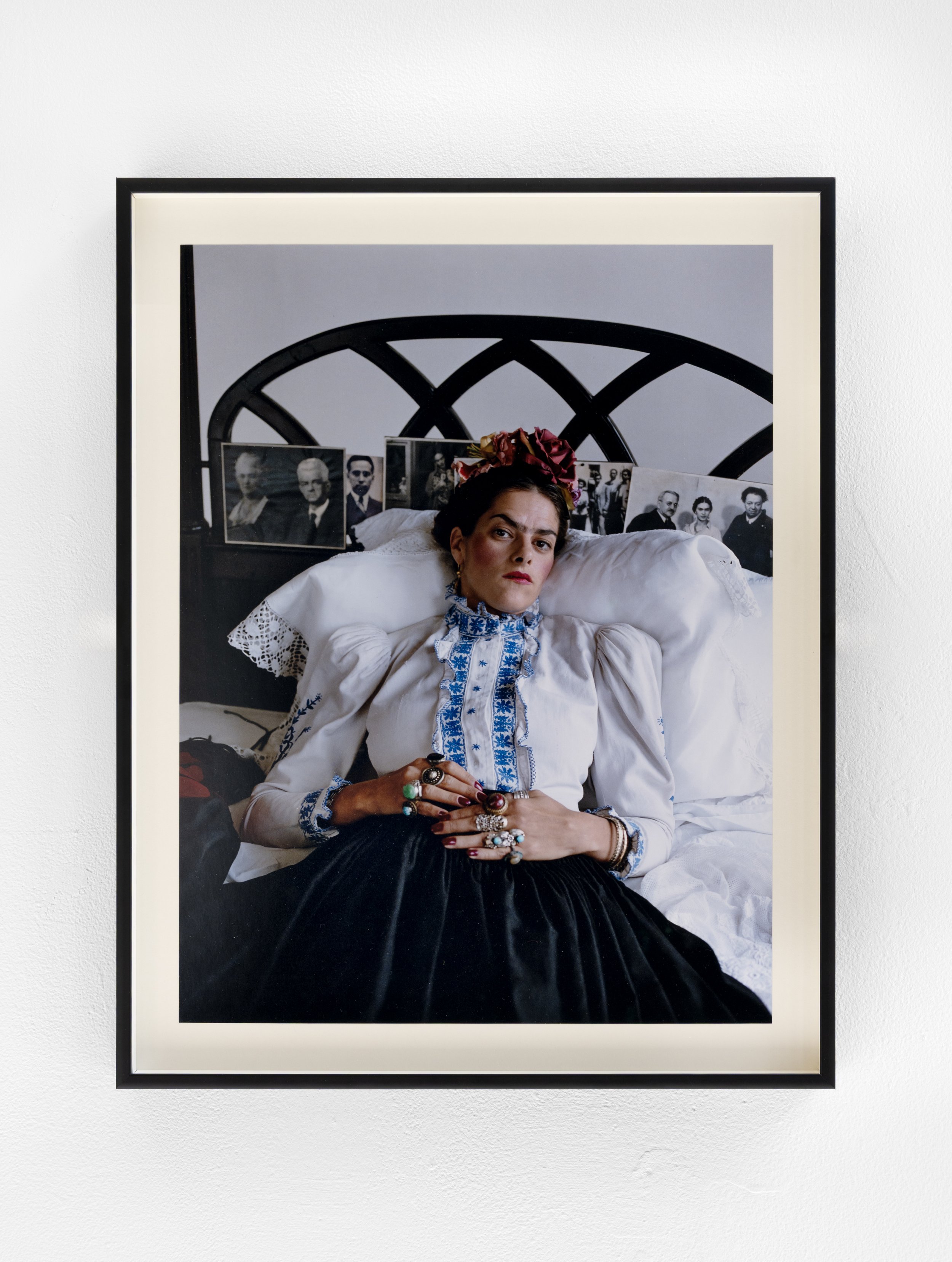 Mary McCartney's 'Tracy Emin as Frida Kahlo' photographed against a white wall in the White Column space. It shows: “Artist Tracey Emin, laid centrally and propped up on white cushions in bed, dressed as painter Frida Kahlo. Staring forward whilst at