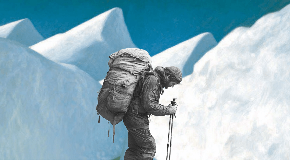 Black and white photo of a man hiking with a large backpack and trekking poles in a snowy mountain landscape.