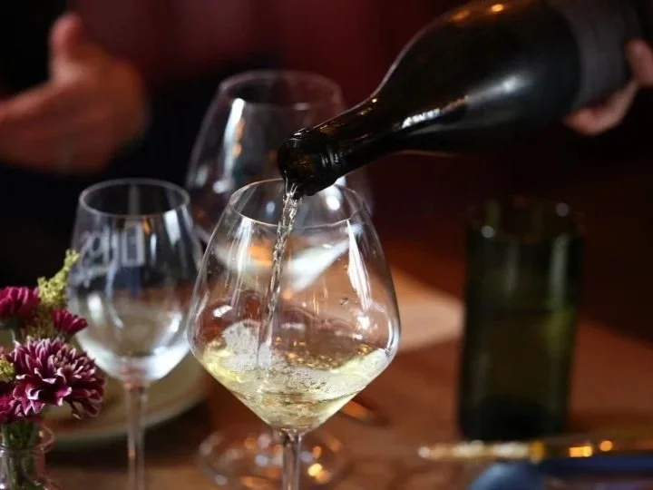 A hand pouring white wine from a bottle into a wine glass at a table at Ethos Wine Bar & Bistro in Downtown Nantucket.