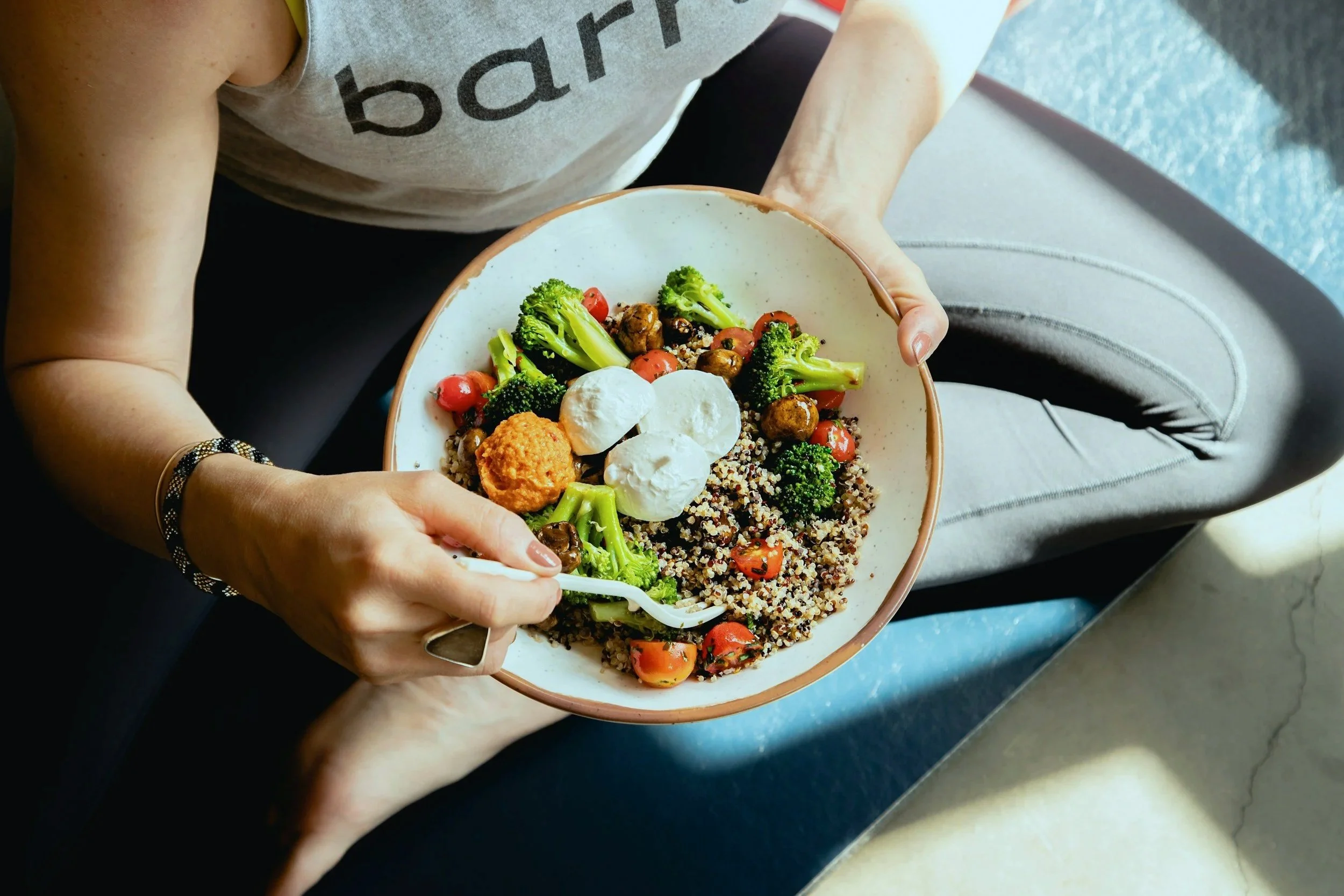 A person holding a bowl of salad with broccoli, cherry tomatoes, quinoa, mozzarella, and a falafel