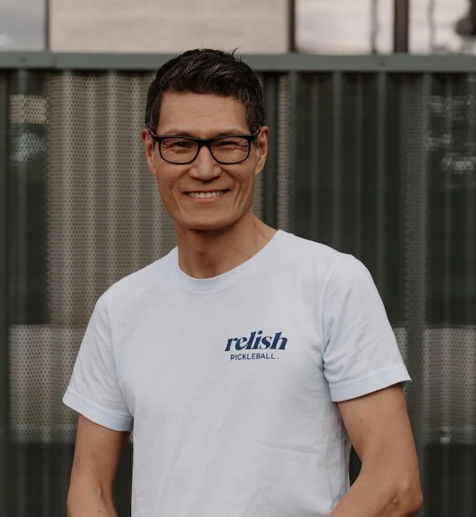 A man standing in front of a green wall, wearing a blue shirt with the logo 'relish' and a name tag that says 'Yuchen'.