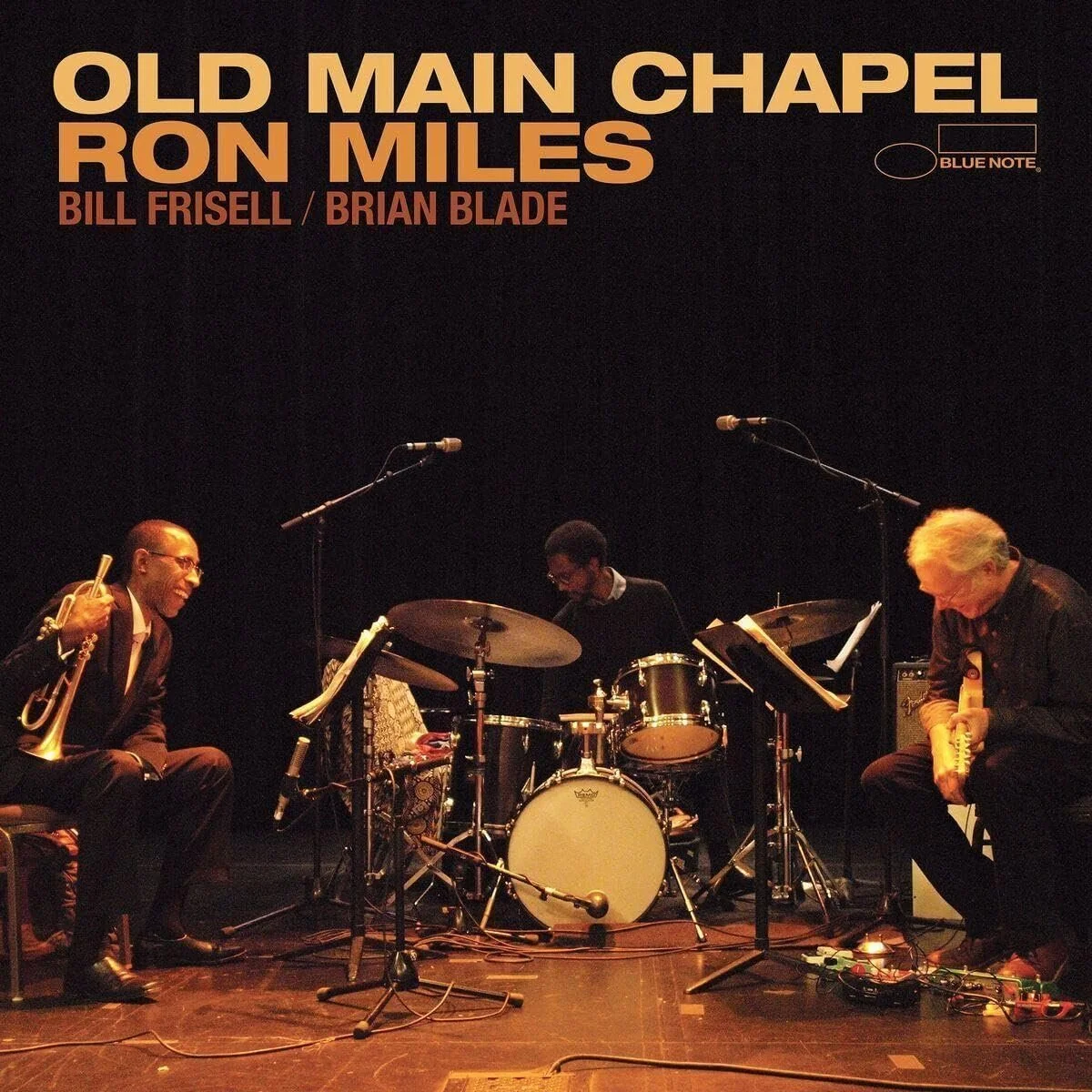 Music album cover titled 'Old Main Chapel Ron Miles' featuring Bill Frisell and Brian Blade, with a photo of three musicians performing with instruments on a stage.