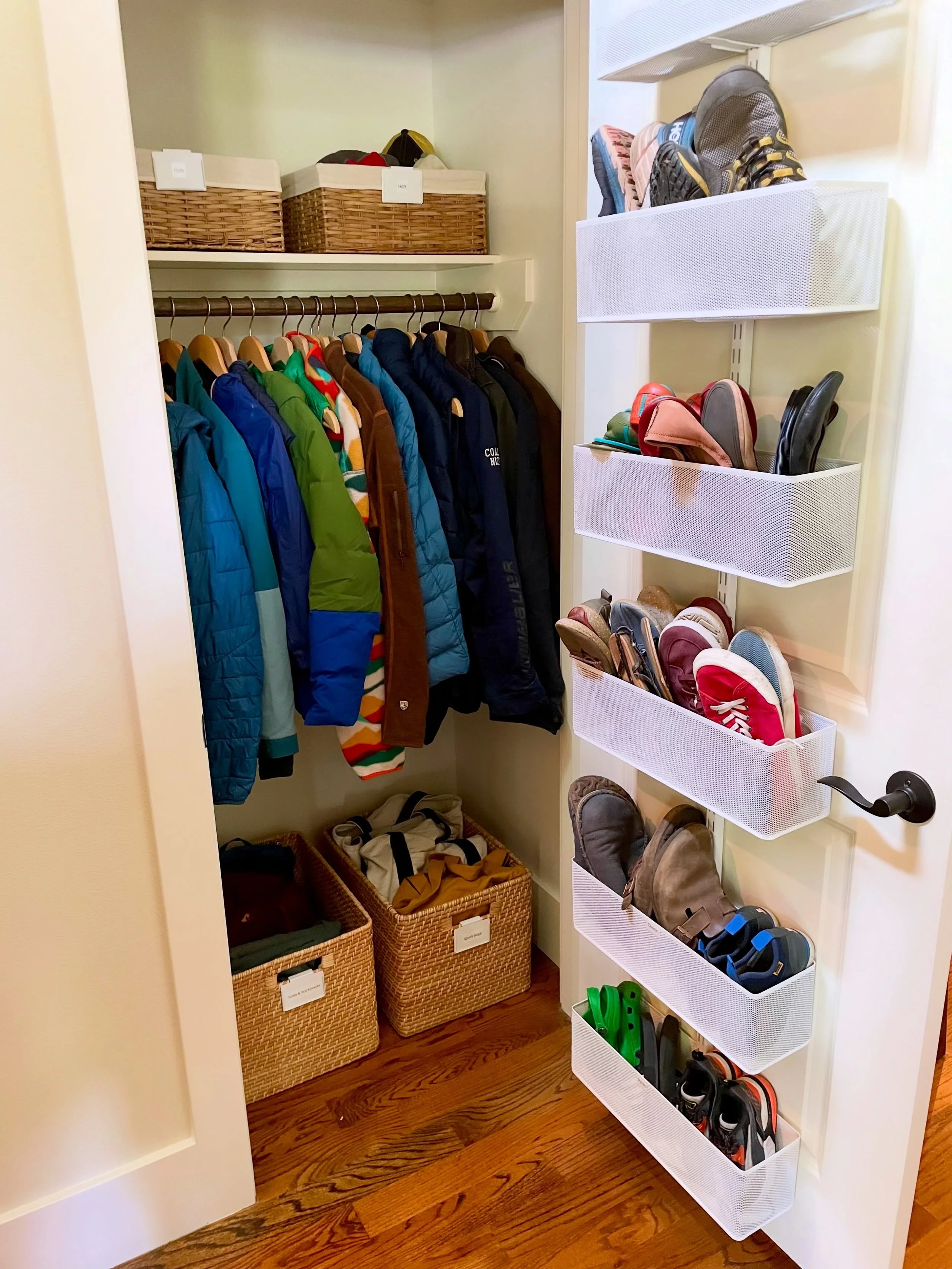 This organized entry closet has 4 key components: 

1. Abundant shoe storage
2. Small baskets for accessories like hats
3. Hanging space for coats and jackets 
4. Large baskets for frequently used bags

Adding this structure makes everything easy for