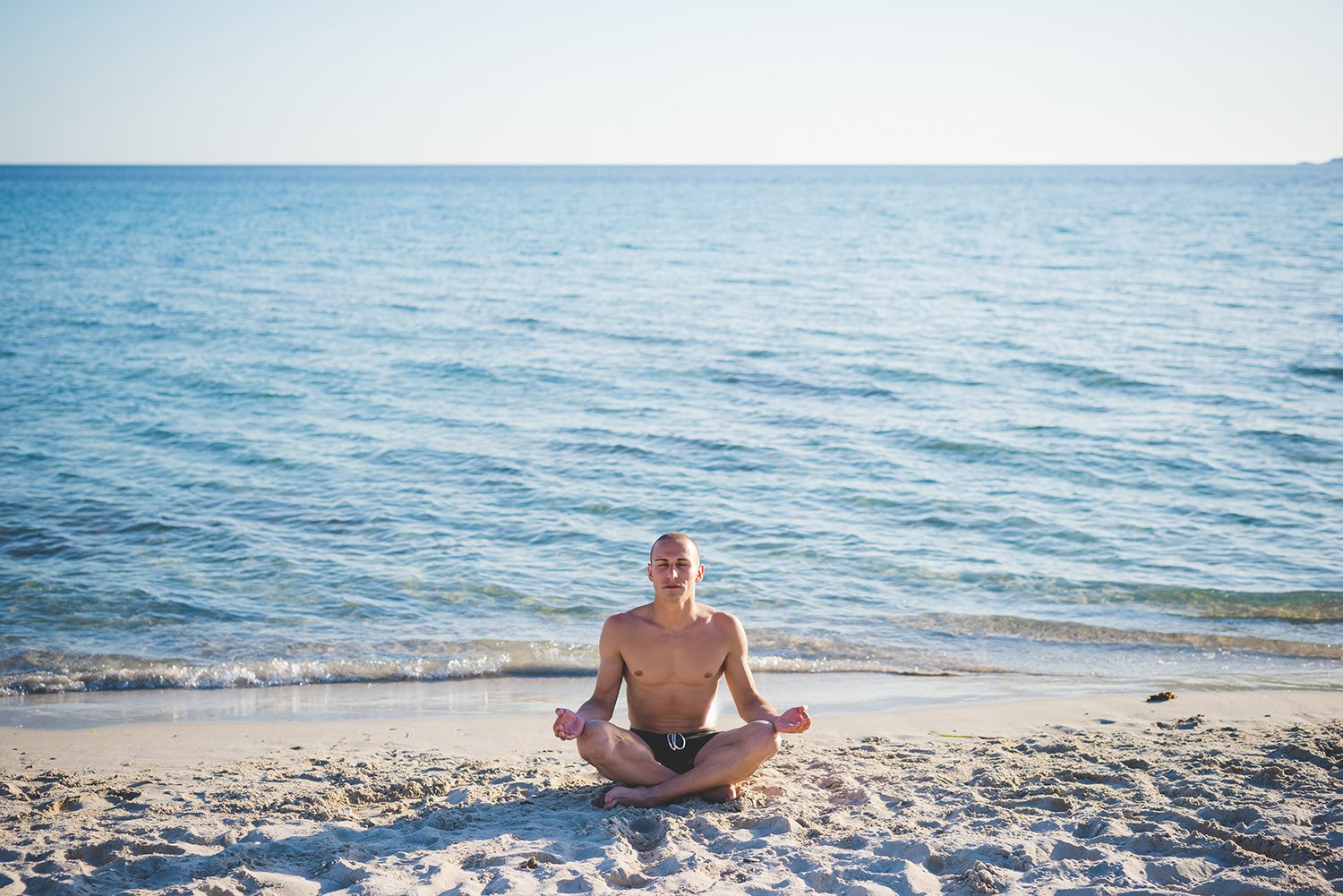 sporty-man-practicing-yoga-at-the-beach-meditation-relaxation-wellness-SBI-304221501.jpg
