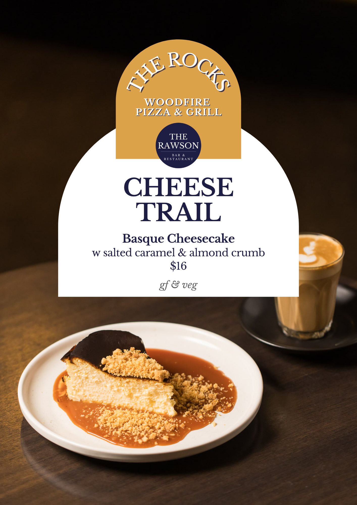 A menu sign advertising a cheese dessert called Cheese Trail, featuring Basque Cheesecake with salted caramel and almond crumb, priced at $16, available as gluten-free and vegetarian. The sign is placed over a table with a slice of cheesecake on a wh