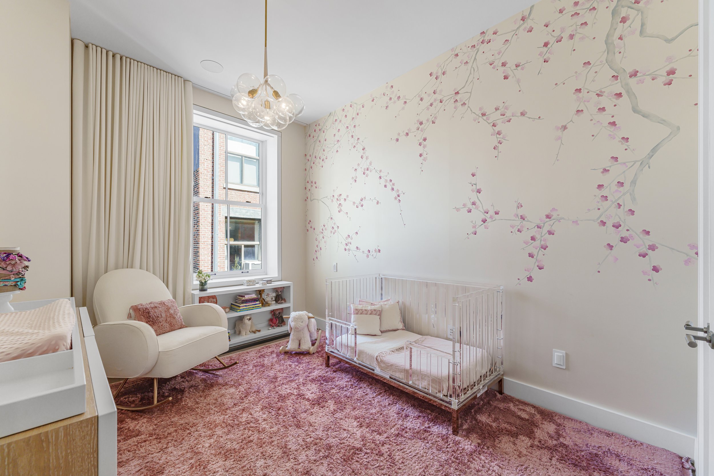Nursery room with floral wall mural, crib, rocking chair, and pink carpet.