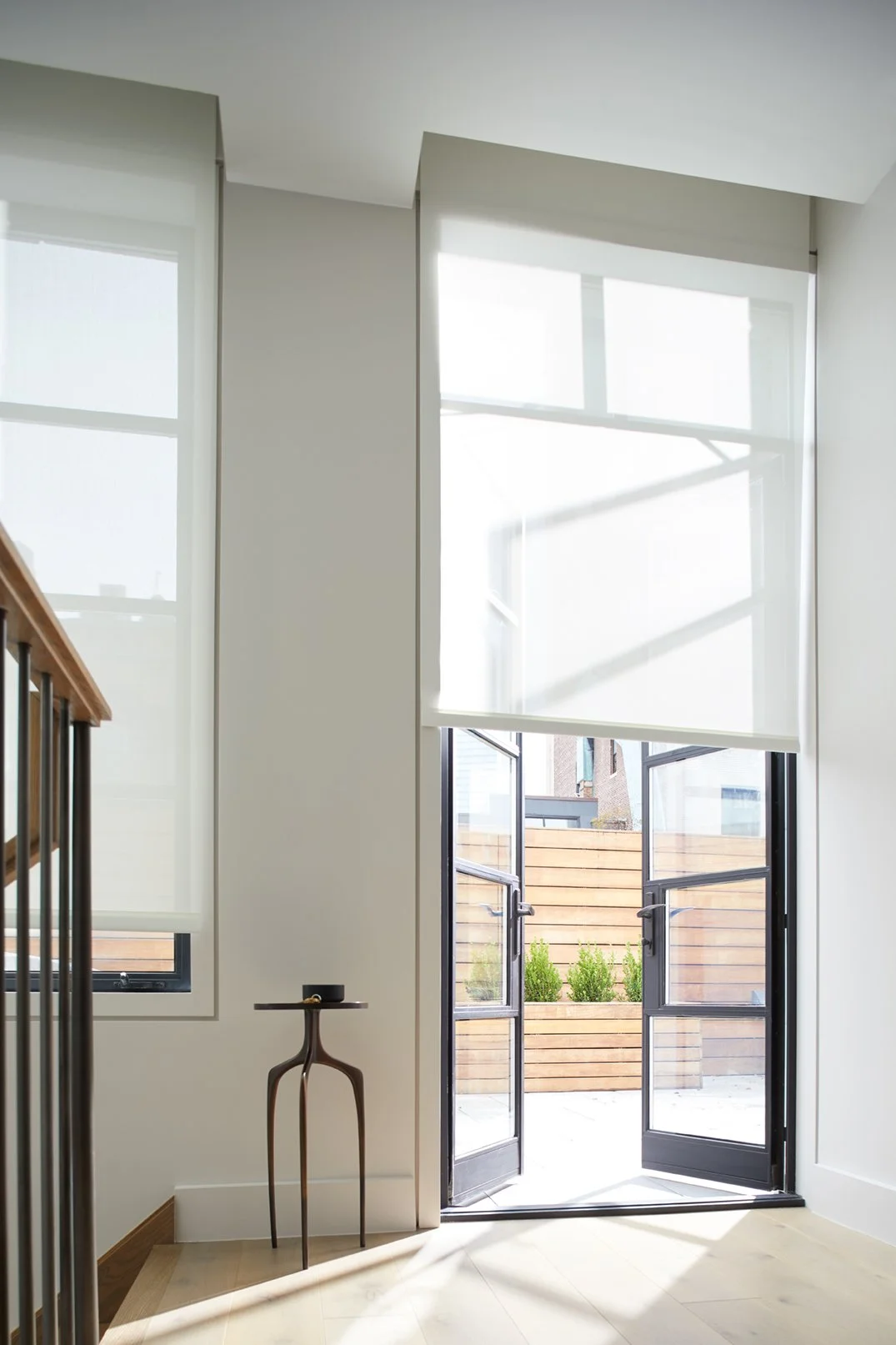 Interior view of a modern room with large windows and a glass door leading outside, with a small wooden side table near the wall.