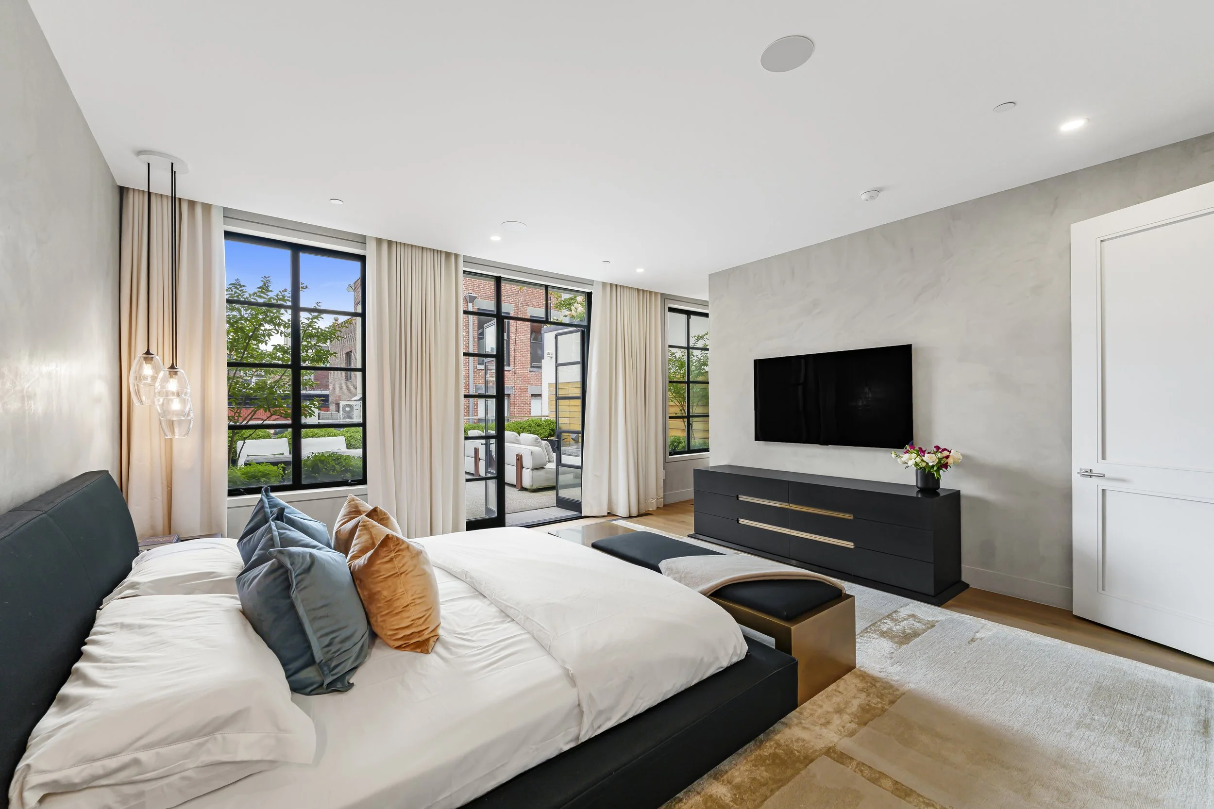 Modern bedroom with a bed, a black dresser, a wall-mounted TV, and large windows with outside view