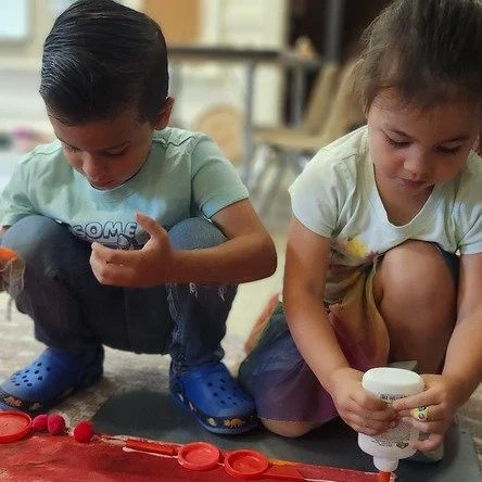 The Pre-K Dragonflies are weaving their Community Banner&mdash;paint dancing on canvas, letters cut from tiny wallpaper worlds, and soon, dragonflies taking flight from loose parts (open-ended treasures like buttons, beads, and wood scraps). Together