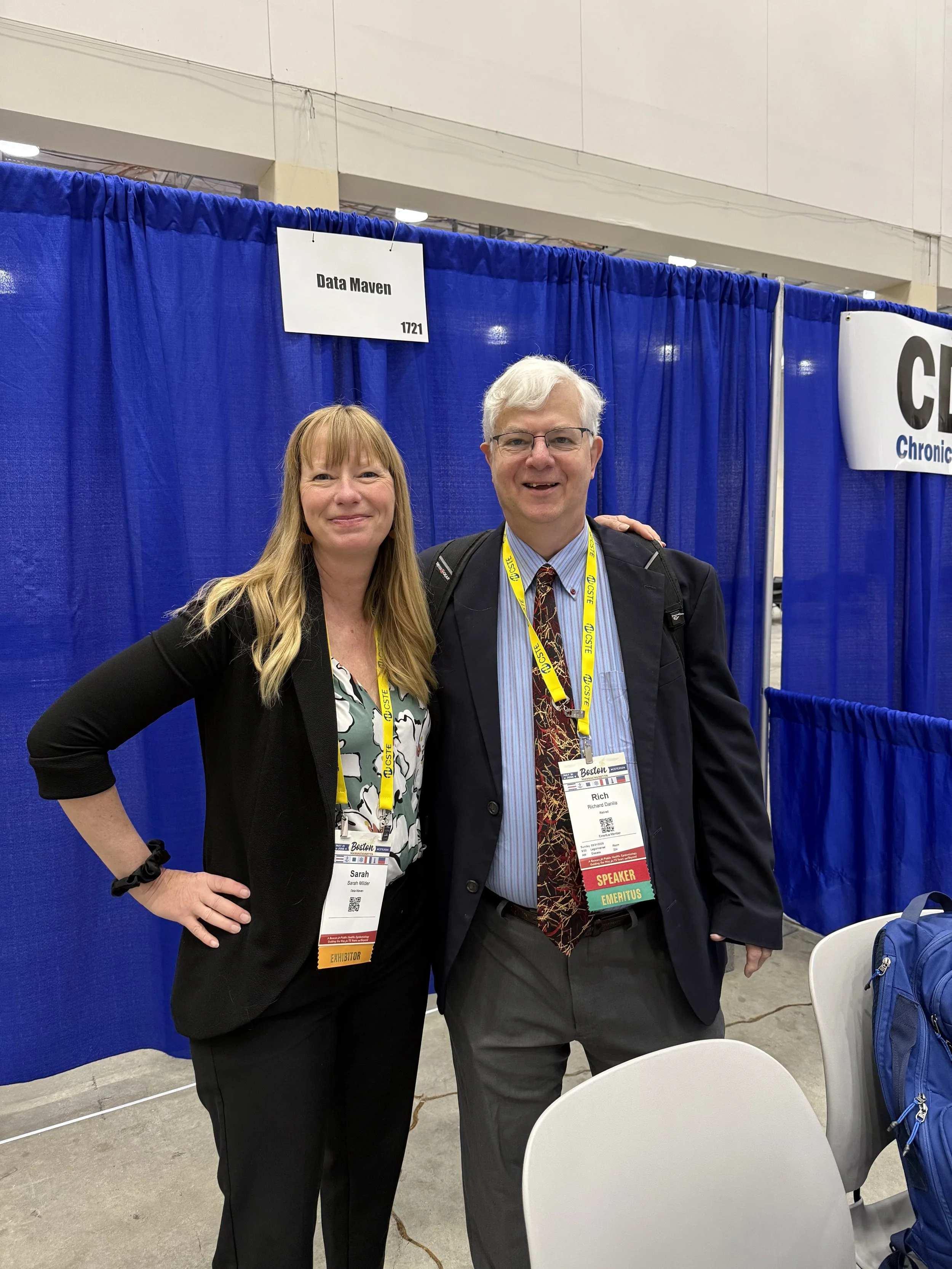 A man and a woman standing together and smiling in front of a Data Maven sign.