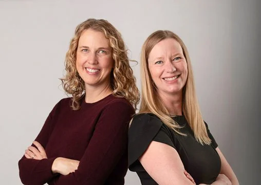 Two women standing back-to-back, smiling.