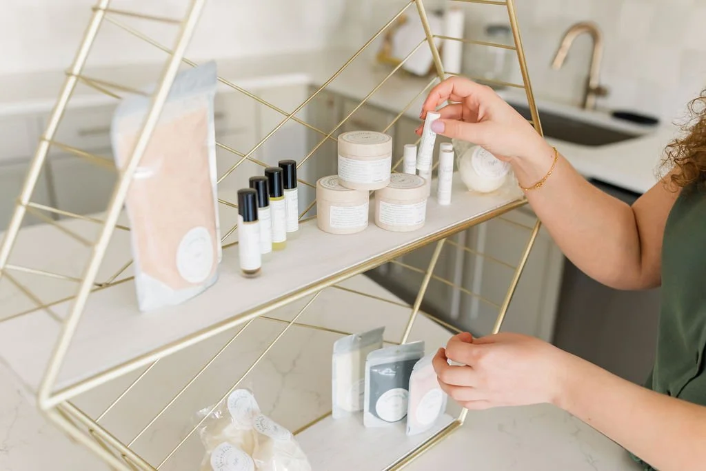 A person browsing Reflect Light Company skincare products on a gold-colored metal display shelf in a bright, modern space.