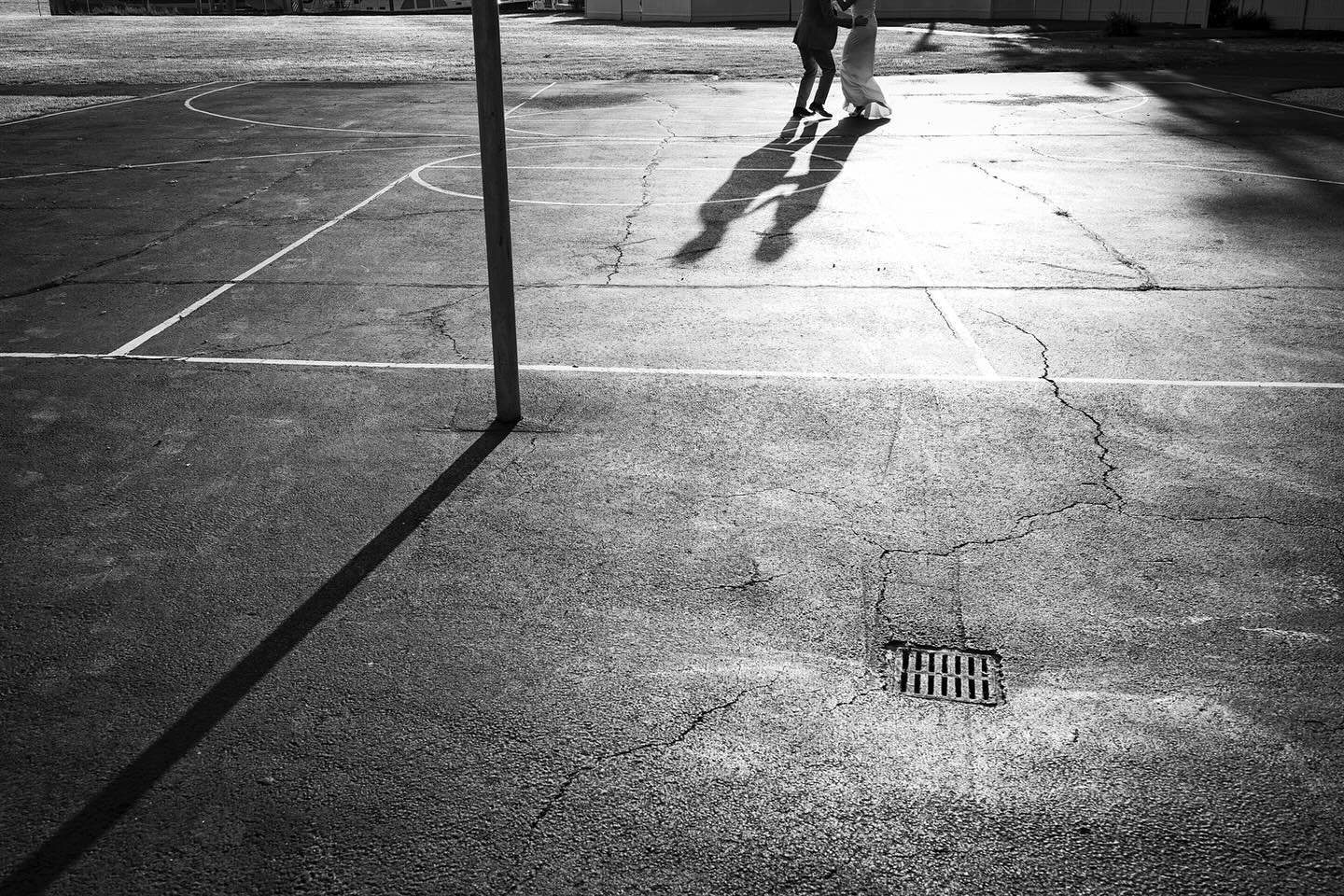 Shadow play as the couple practice their first dance on a basketball court away from their reception.