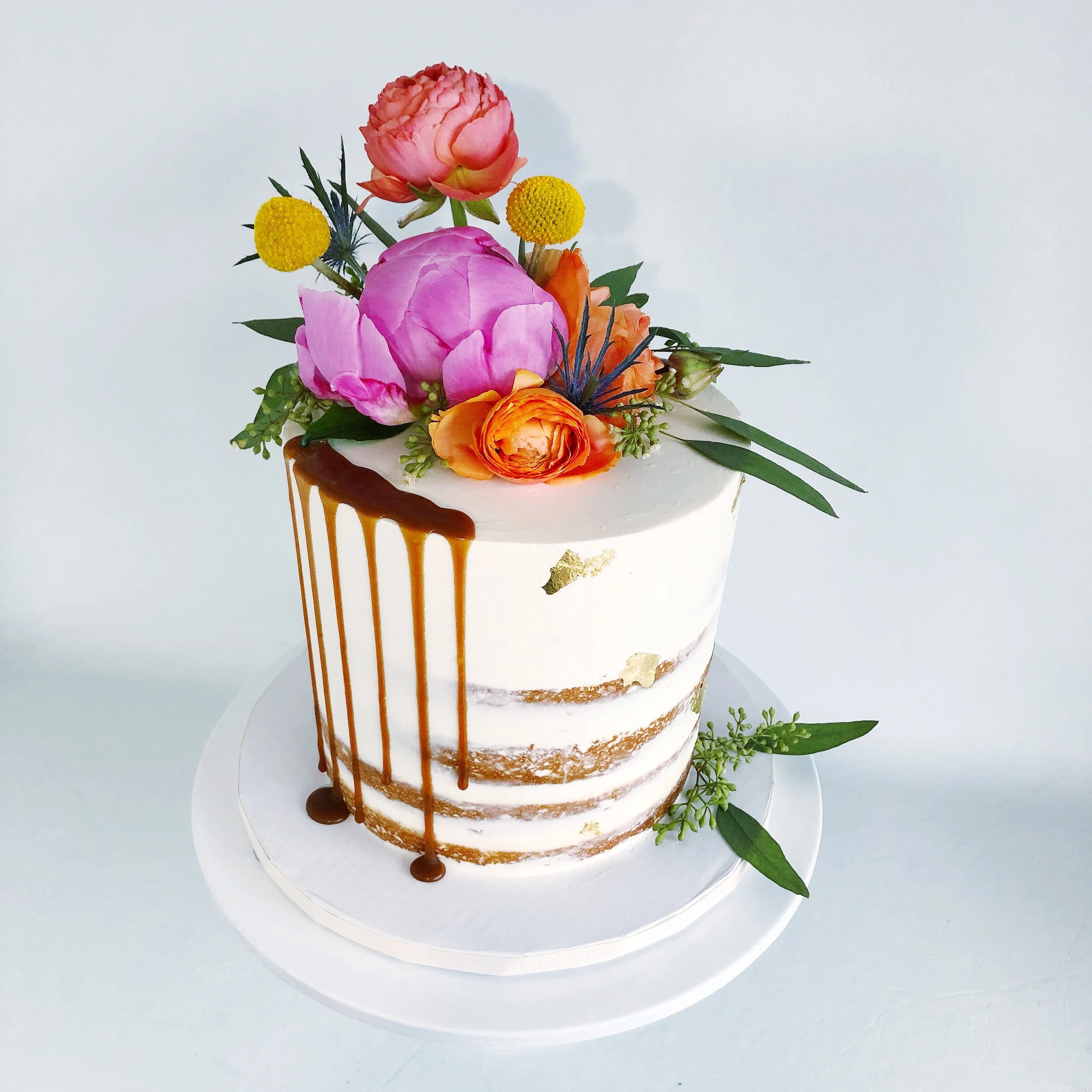 Semi-naked design with gold leaf flecks, caramel drip, and fresh flowers
