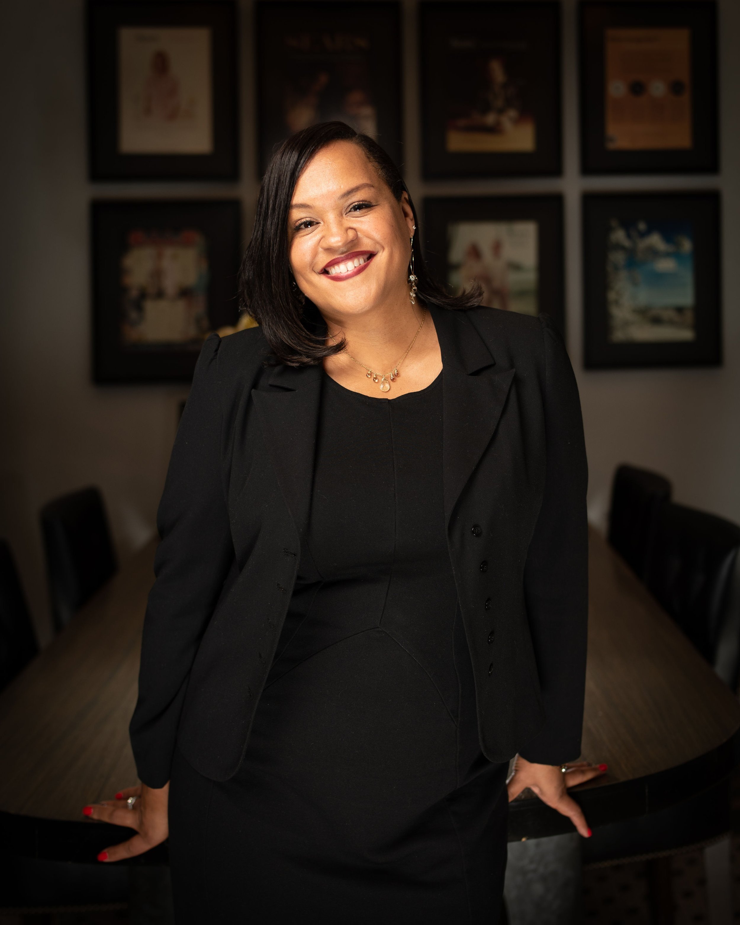 Smiling person in black suit standing in front of framed wall art