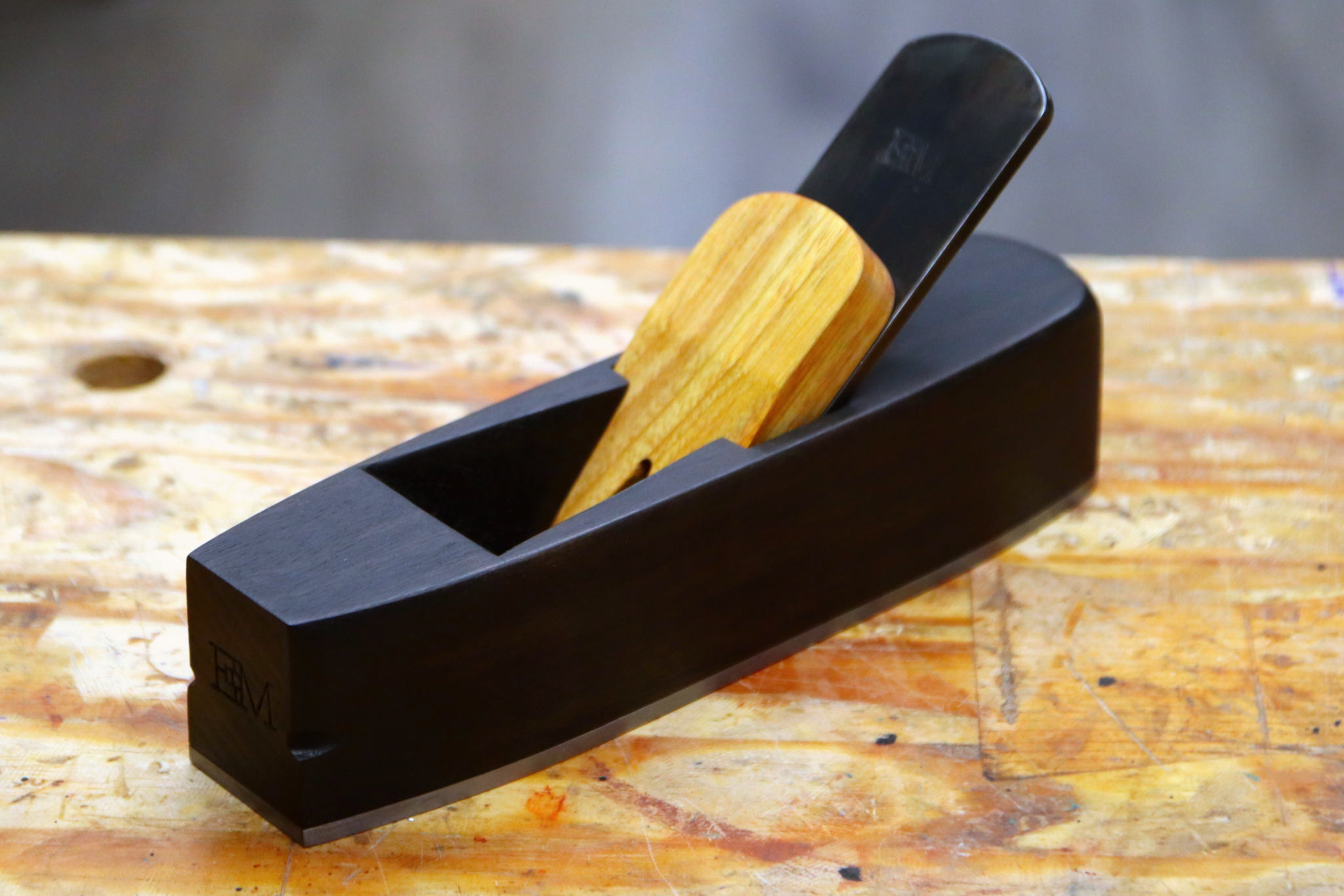 A miter plane made from ebonized canary wood sitting on a workbench.