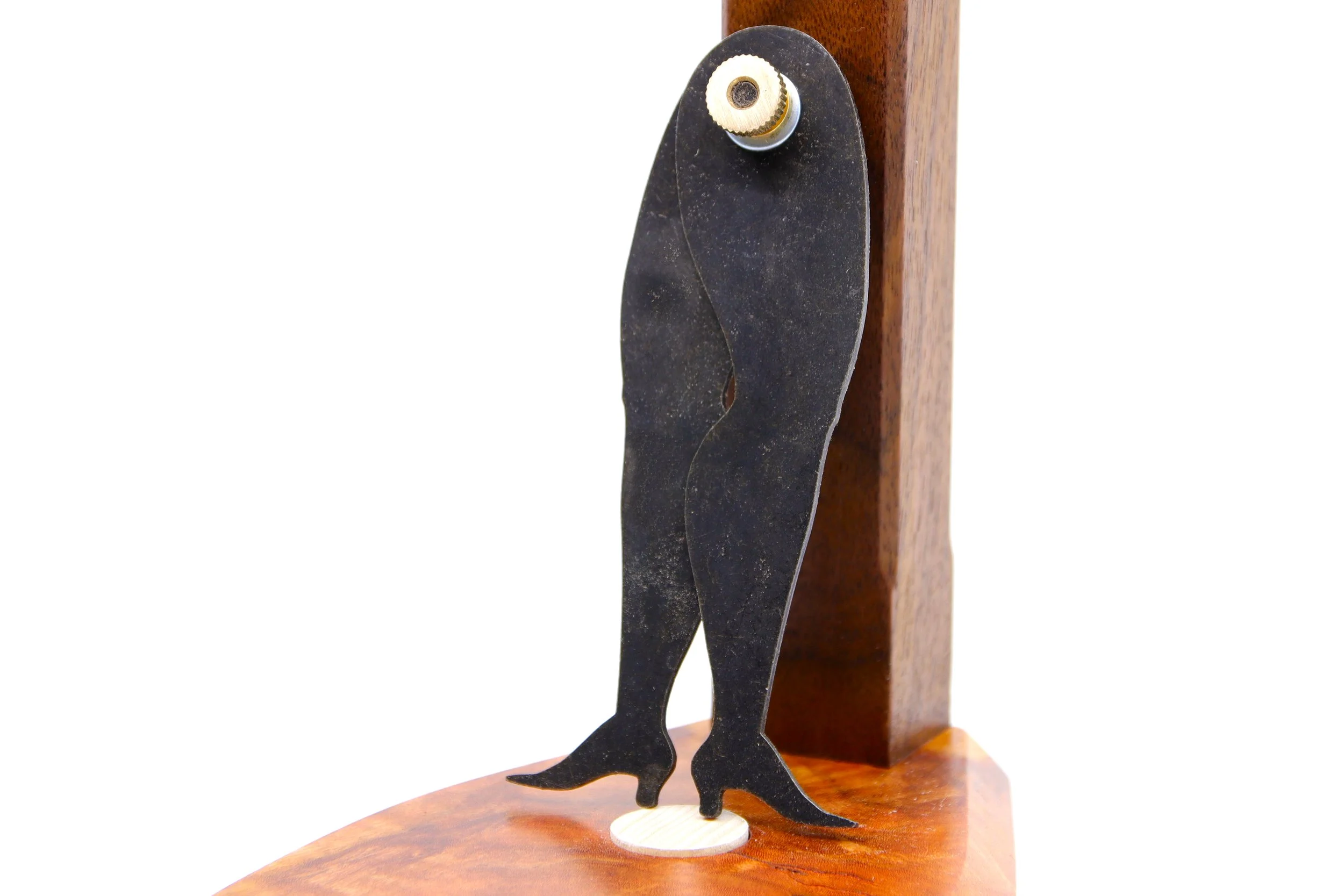 Legs with high-heeled boot shaped caliper propped up against a piece of burled walnut stand.