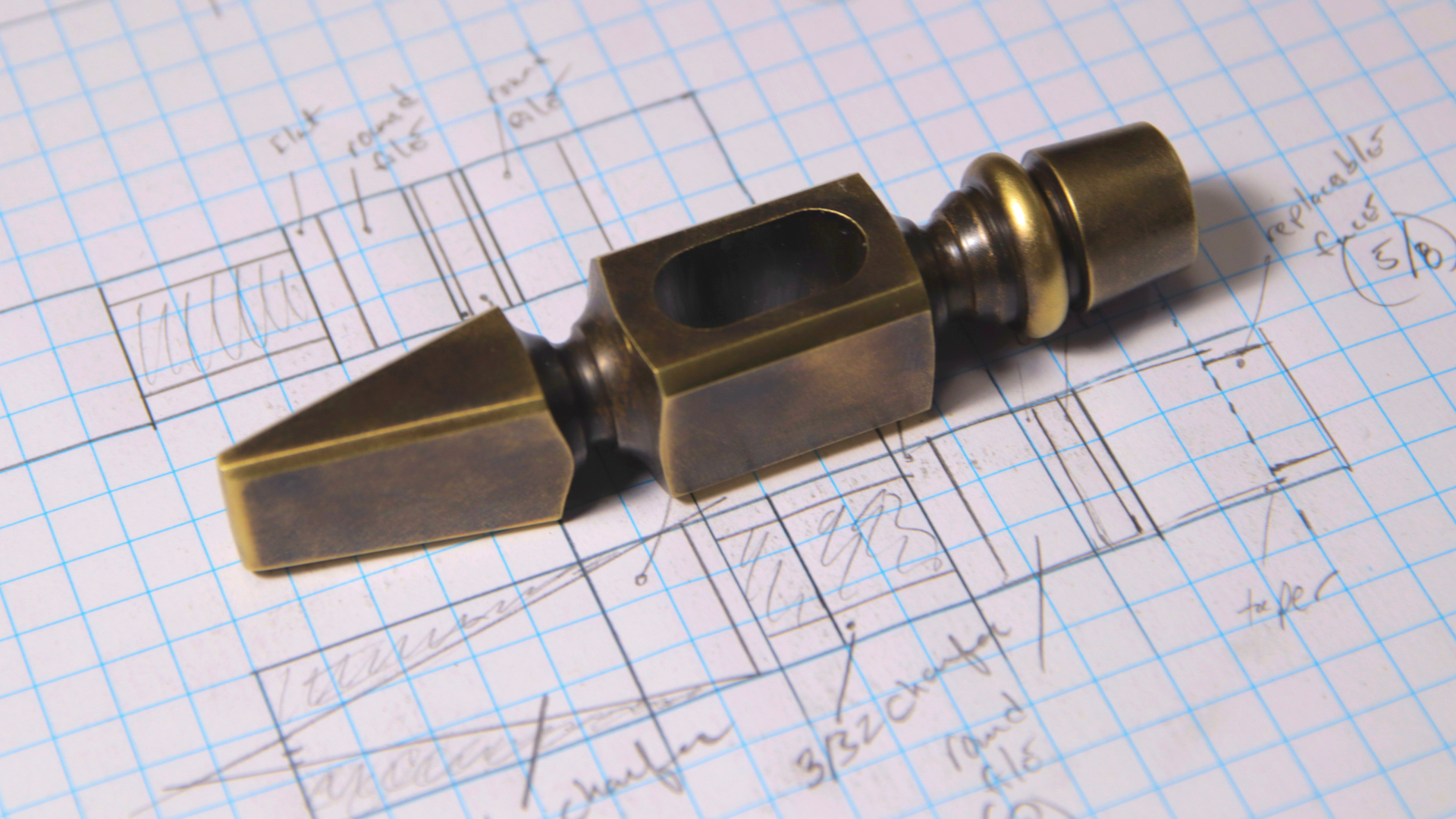 Carved brass hammer head sitting on a set of blueprints.