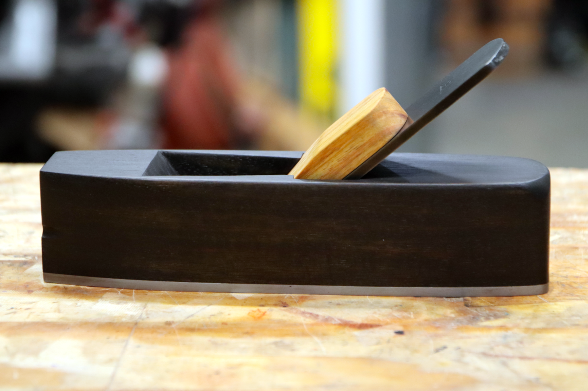 A miter plane made from ebonized canary wood sitting on a workbench.