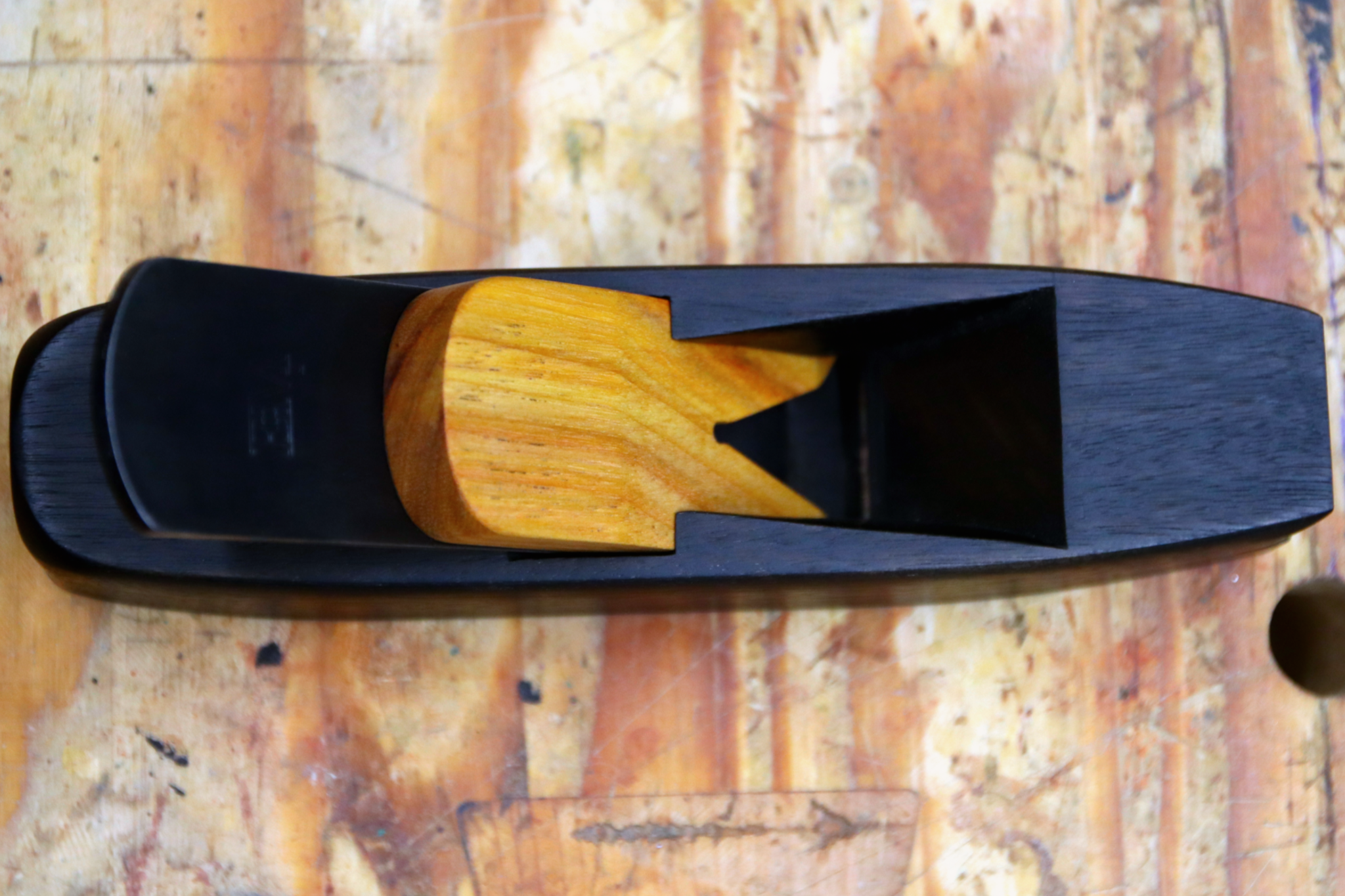 A miter plane made from ebonized canary wood sitting on a workbench.