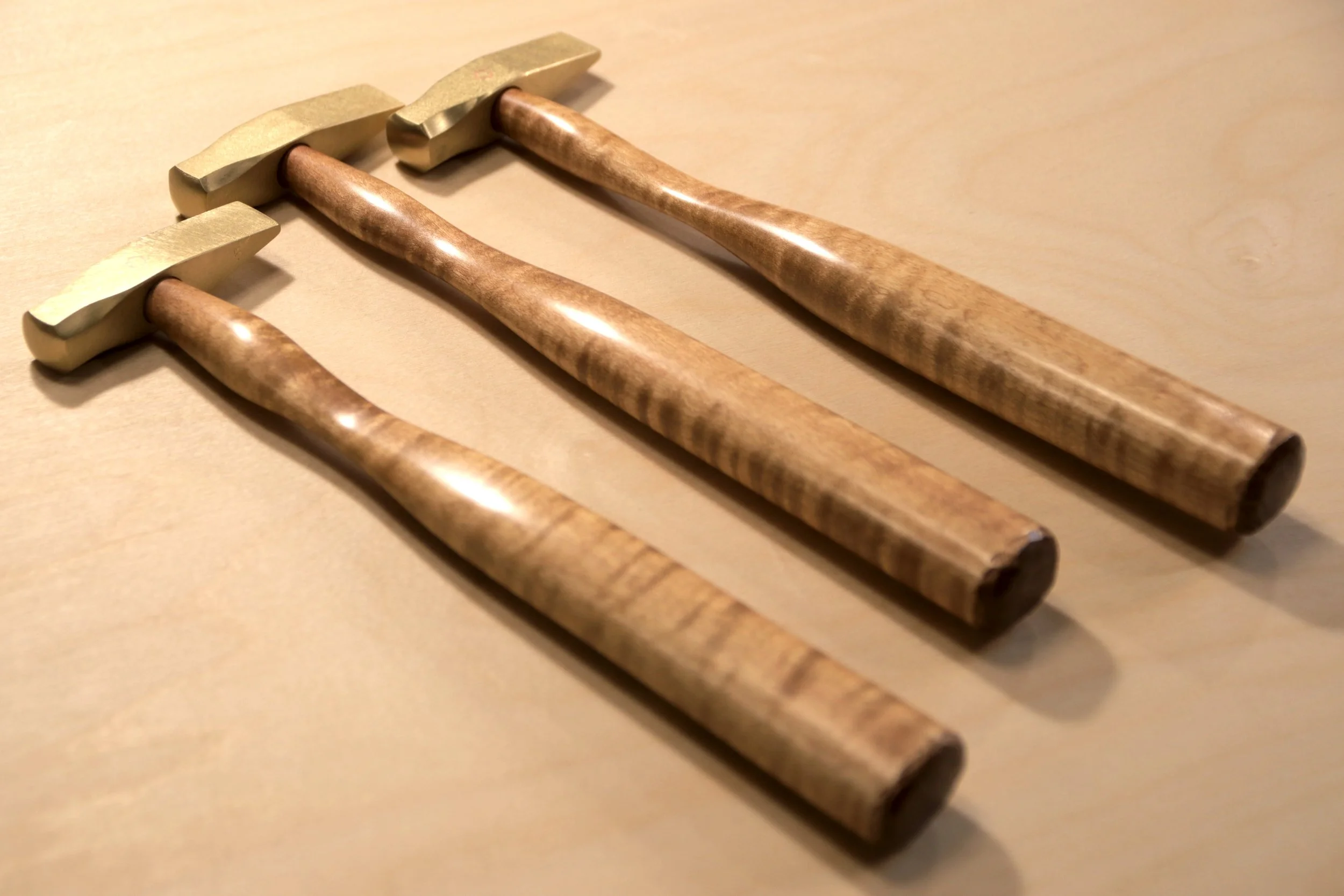 Three brass hammers with curly maple handles.