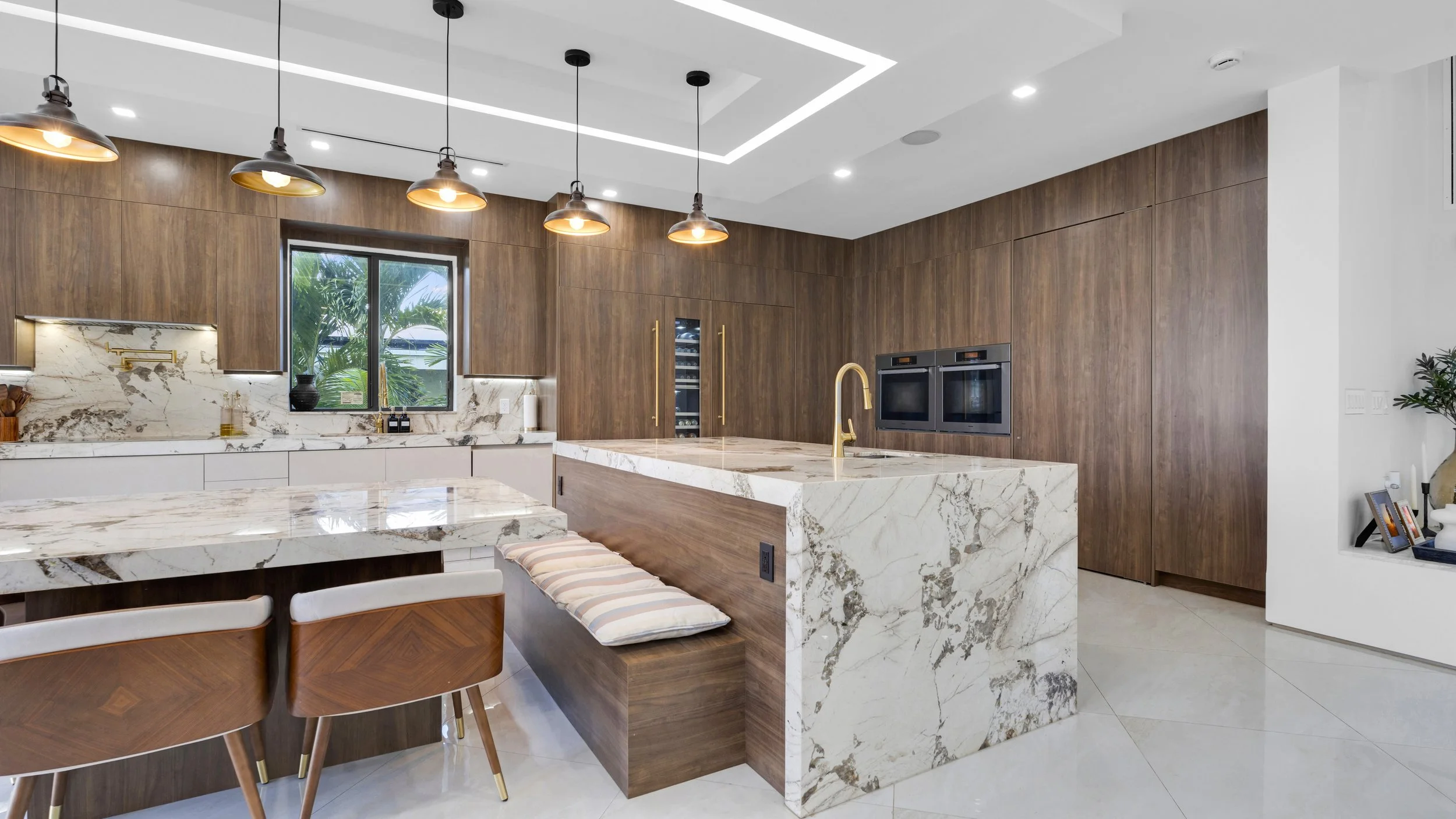 Modern kitchen with marble island and backsplash, wooden cabinets, and black pendant lights.