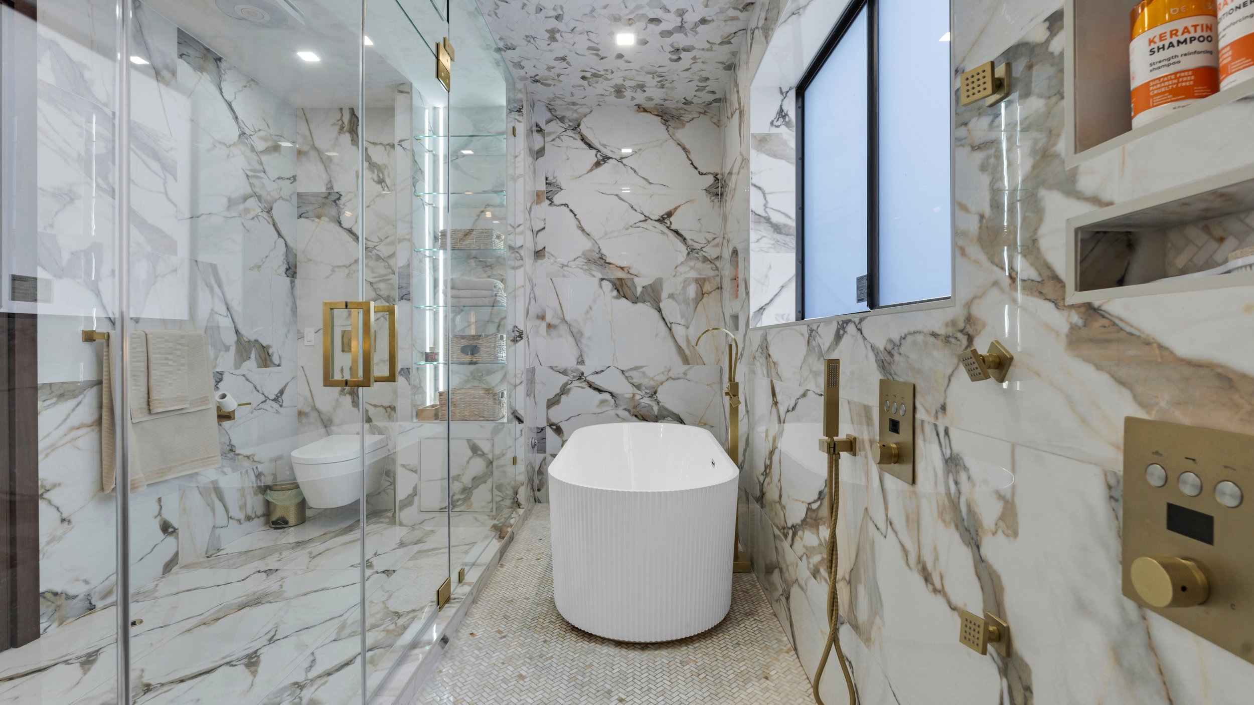 Luxury bathroom with marble walls and floor, gold fixtures, and a freestanding bathtub.