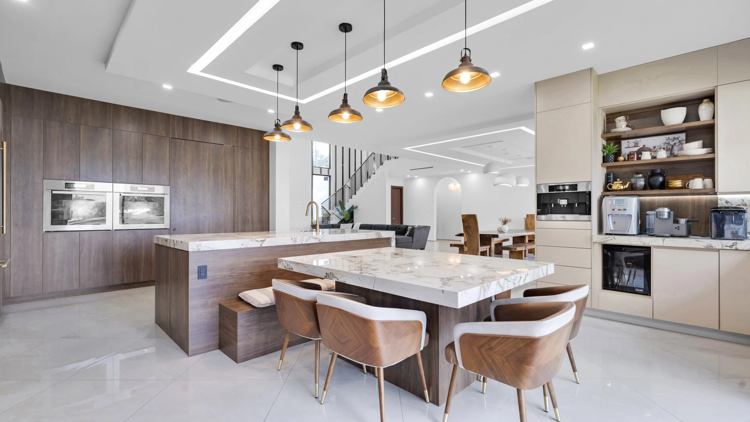 Modern kitchen with marble countertops, wooden cabinets, and pendant lighting, open to a living and dining area.