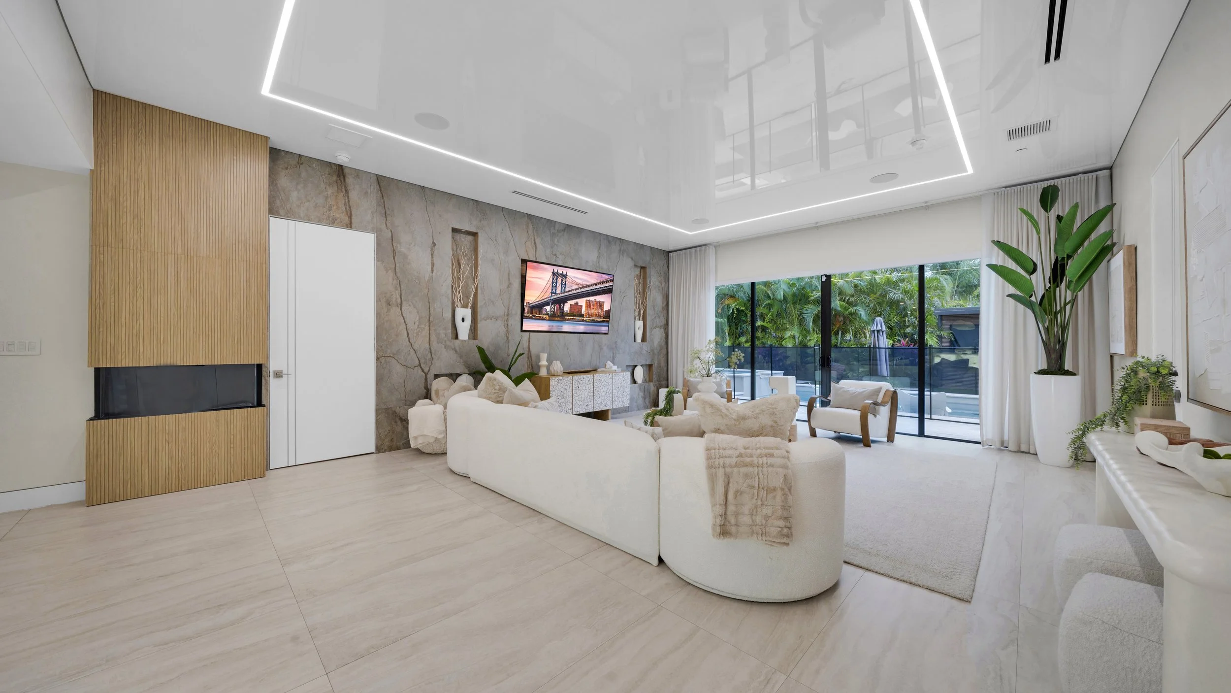 Modern living room with large sliding glass doors leading to outdoor patio, white curved sofas, armchairs, decorative vases, and a large potted plant, with ceiling LED lighting and a marble accent wall.