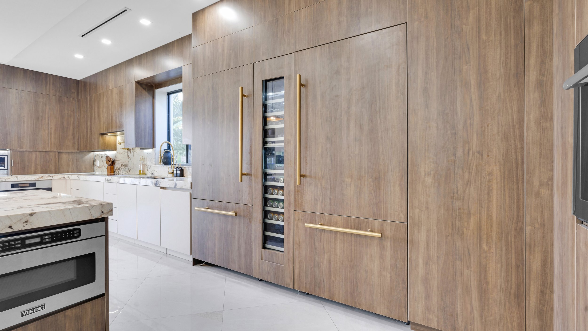Modern kitchen with wooden cabinets, white marble countertops, a built-in oven, and a wine refrigerator with a glass door.