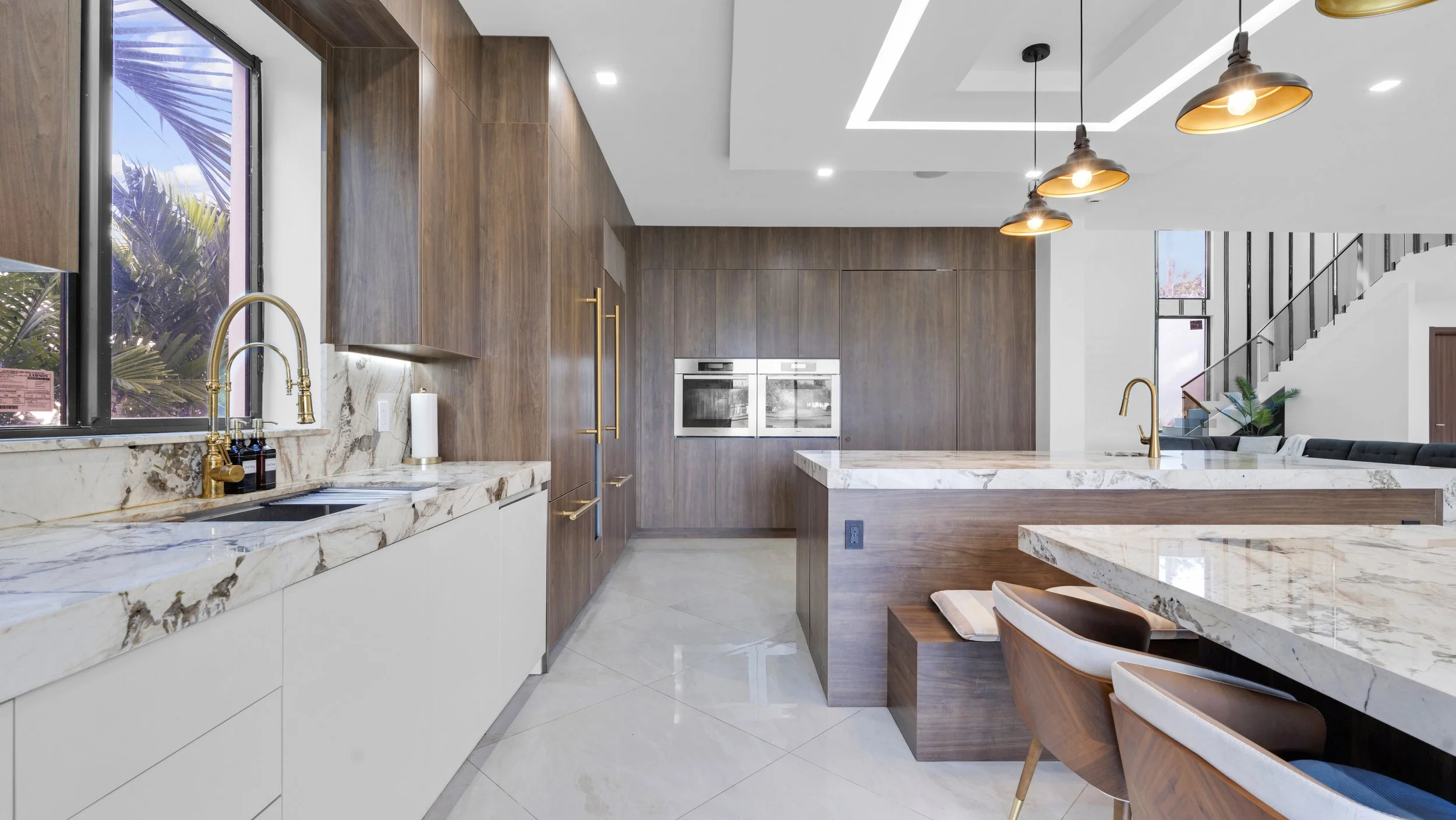 Modern kitchen with wooden cabinets, marble countertops, gold fixtures, and pendant lights.