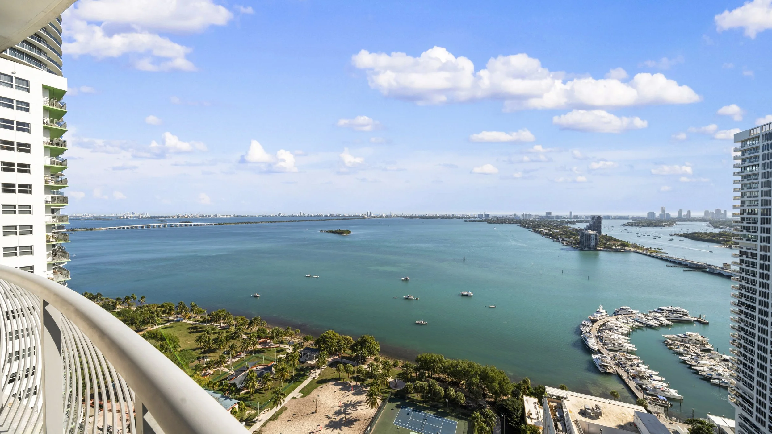 View of a large body of water with boats, high-rise buildings, and a coastal city skyline under a blue sky with scattered clouds.