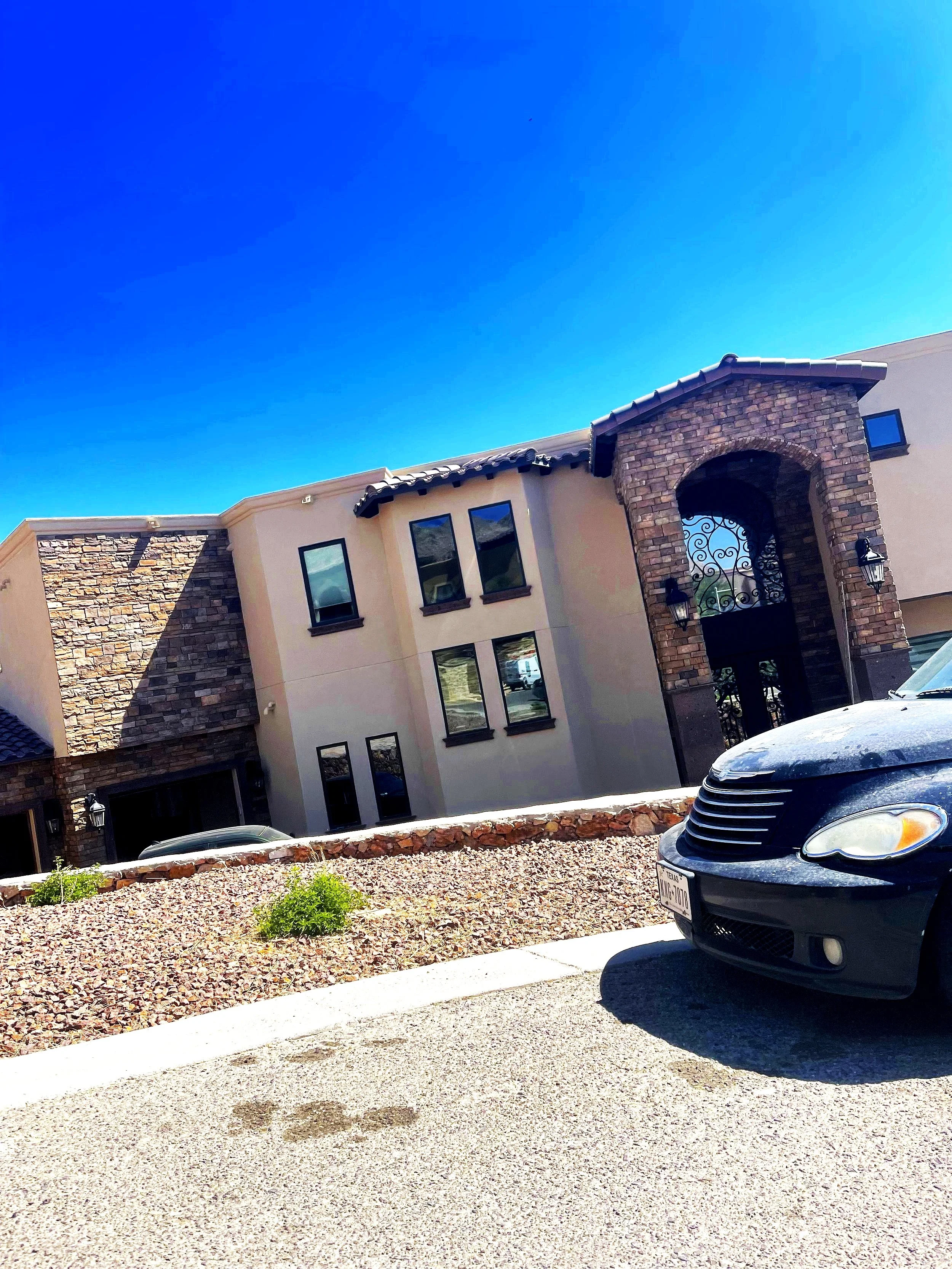 Modern house with stone accents and arched entryway, parked car in foreground, blue sky above.