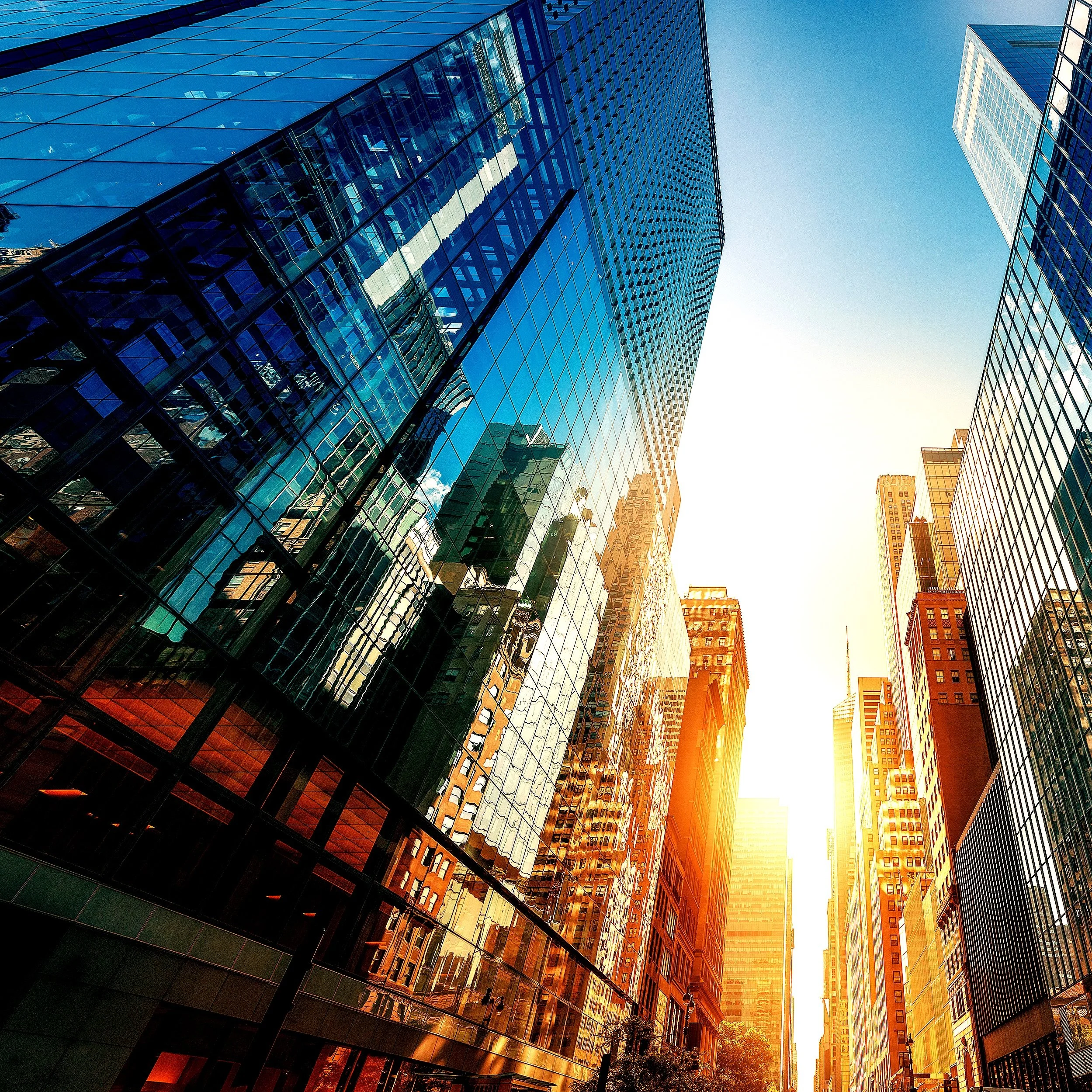 Urban cityscape with tall glass skyscrapers reflecting sunlight, featuring a clear blue sky and modern architecture.