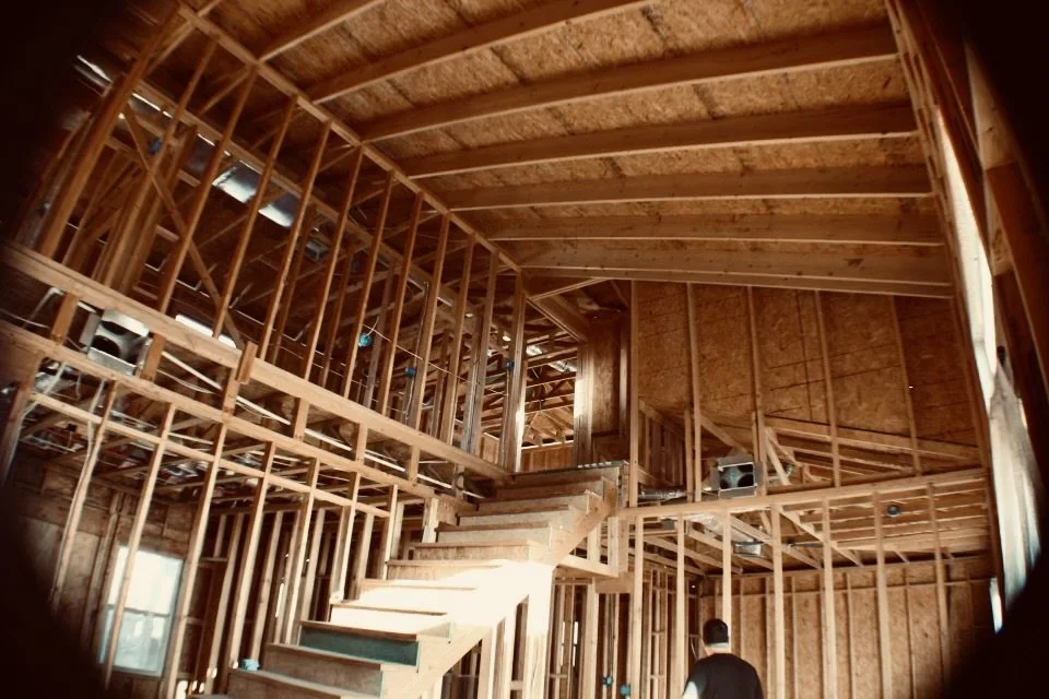 Residential construction site showing unfinished wooden framing and a partially built staircase.