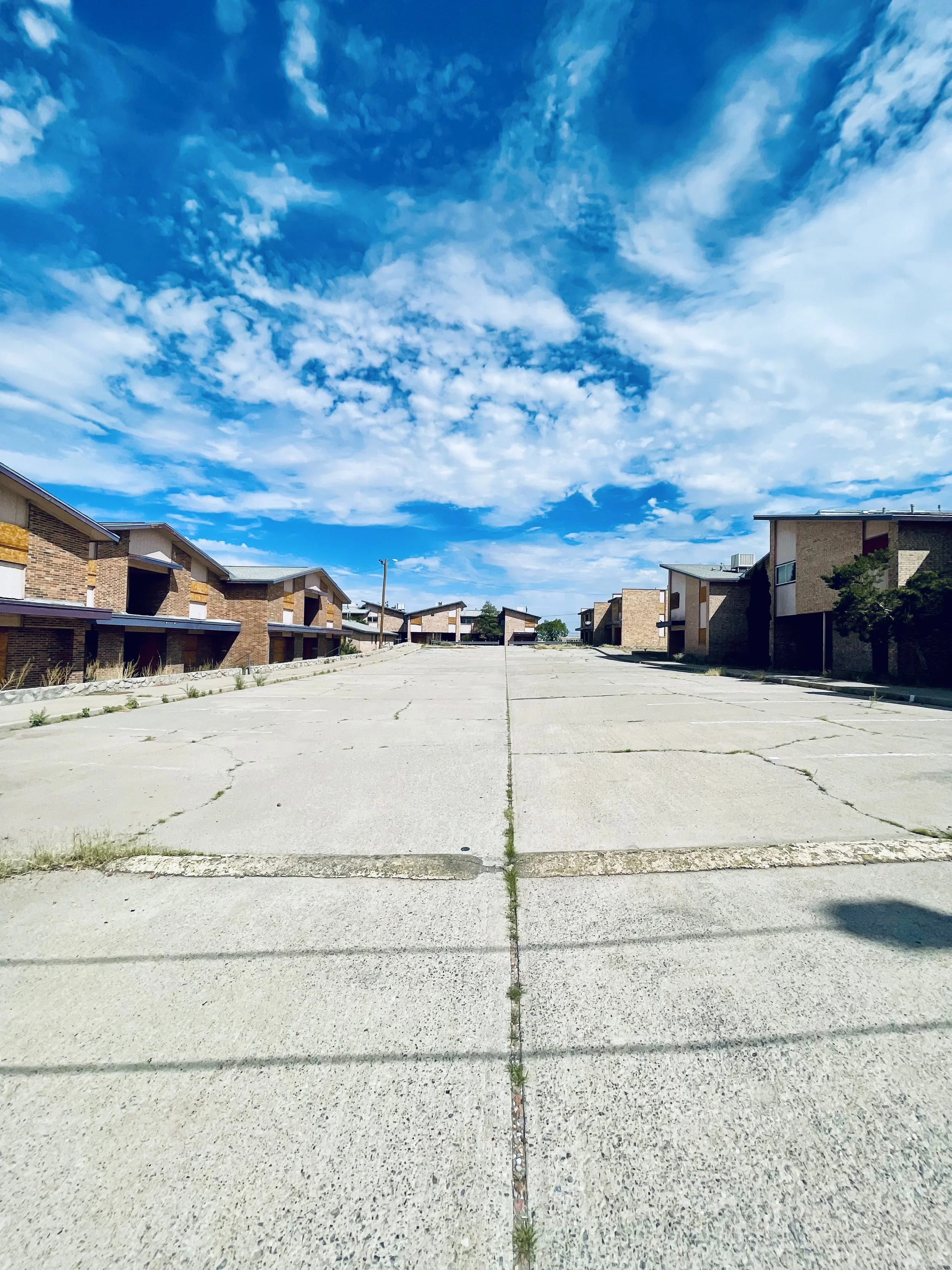 Empty street with buildings on either side under a blue sky with clouds.