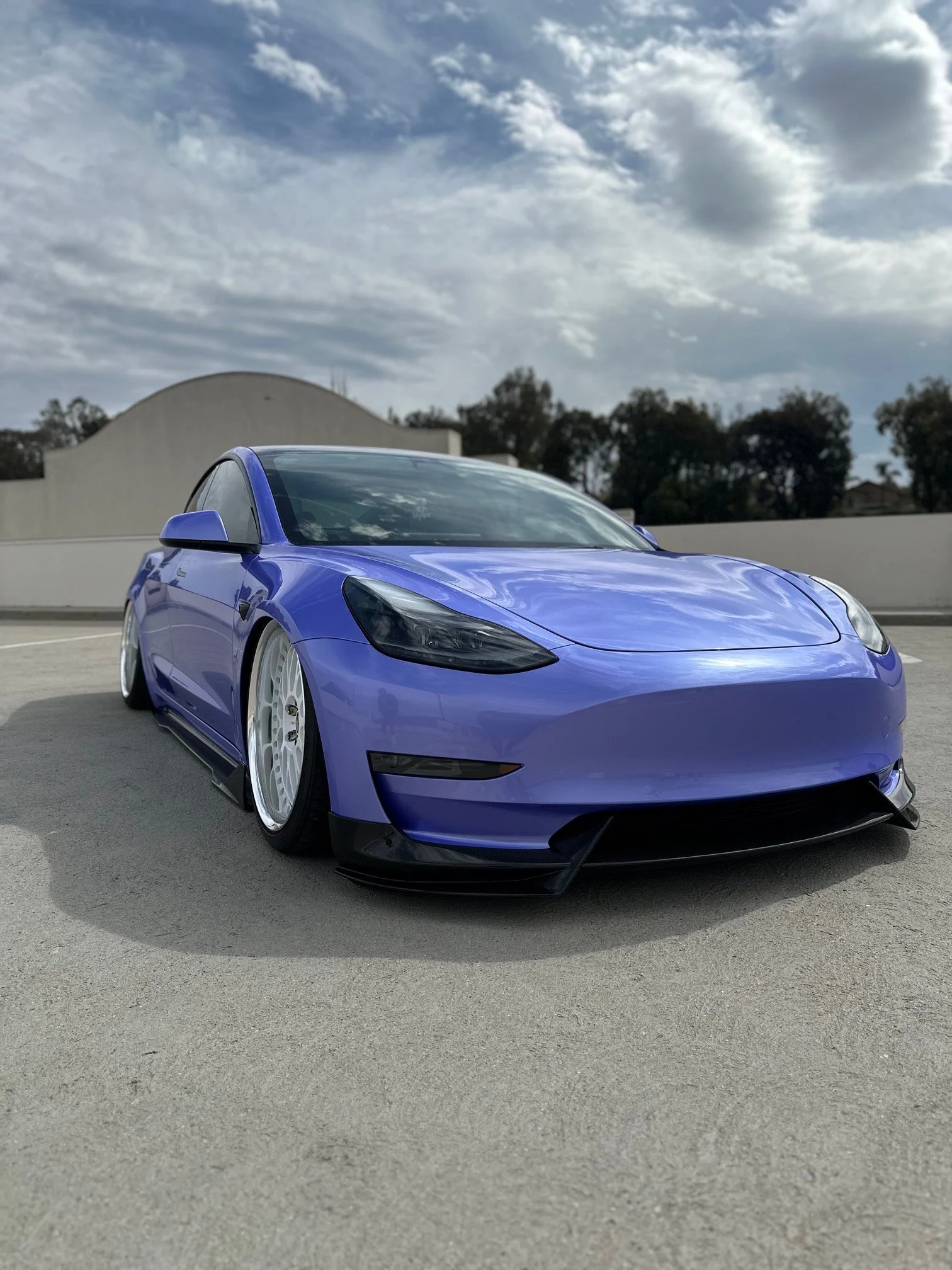 A purple sports car parked on a rooftop with a cloudy sky in the background.