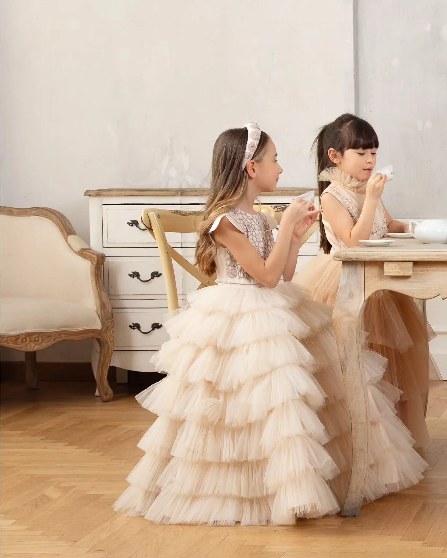 In a quiet room where whispers turn into stories, two little souls share laughter and warmth over tea. 
The moment feels like a page from a storybook gentle, timeless, and beautifully woven in soft elegance.

[L&agrave;TaRa | Hand embroidered dress |