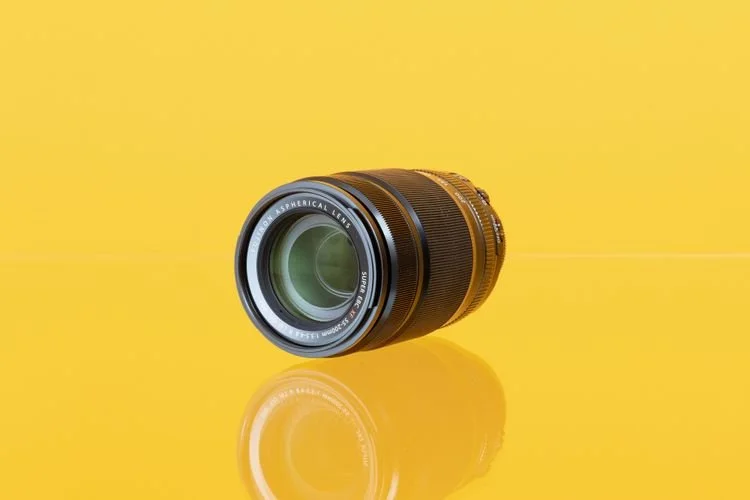 A camera lens placed on a yellow surface with a yellow background, showing the front element and lens markings.