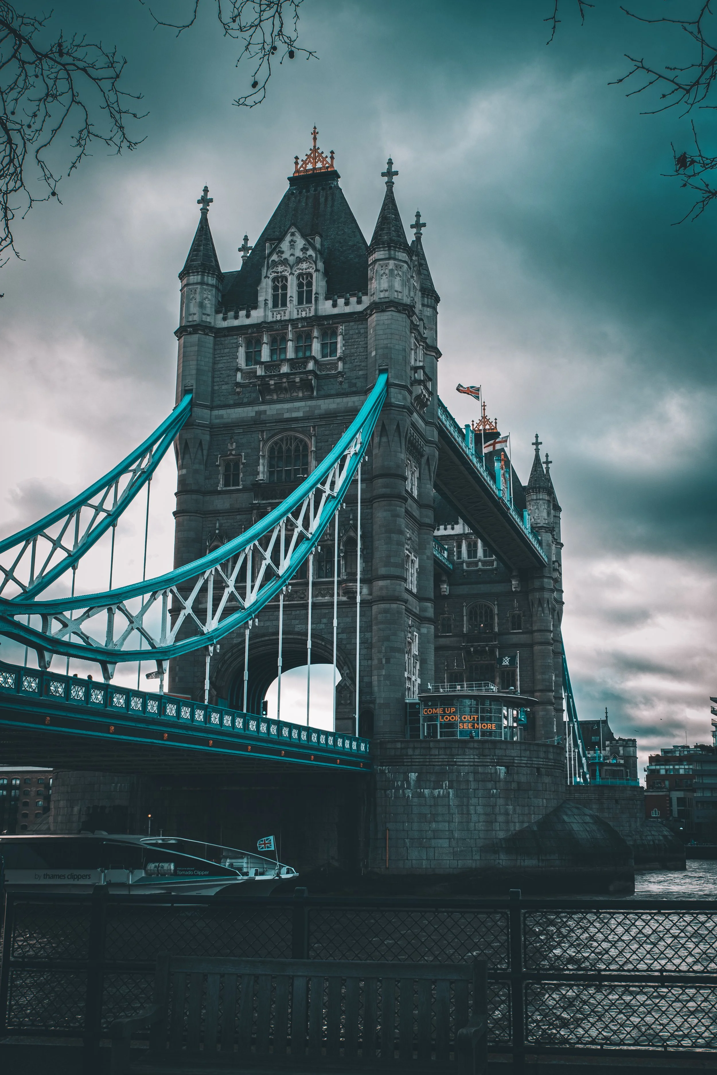 London's Tower Bridge over the River Thames with cloudy sky, featuring two towers with gothic architecture and suspension cables, scene set in the late afternoon.