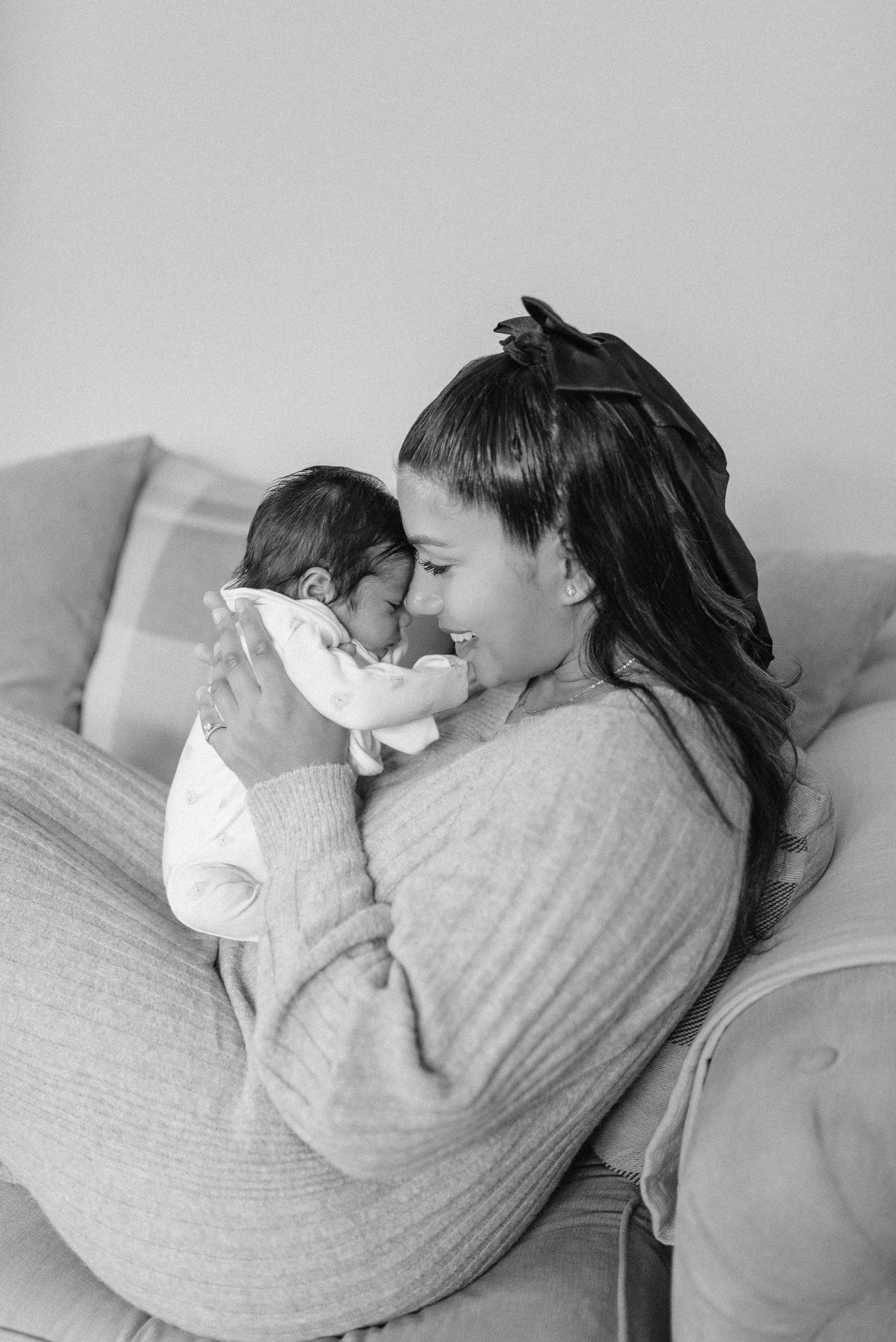 Norfolk Family Photographer.  A woman holding a newborn baby close in an embrace, smiling in a cozy setting.